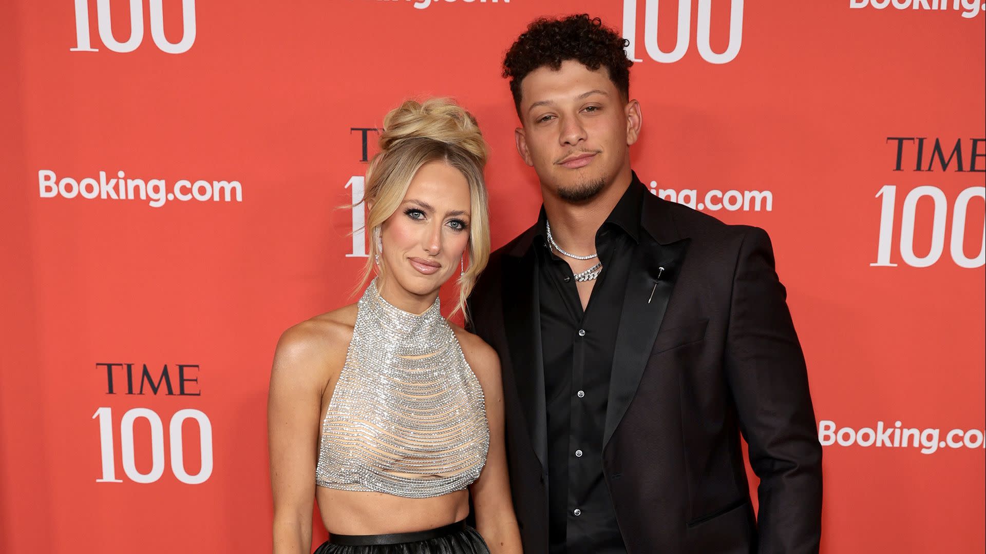 A man and woman pose on the red carpet at the TIME 100 event. The woman wears a sparkling top, and the man is in a dark suit.