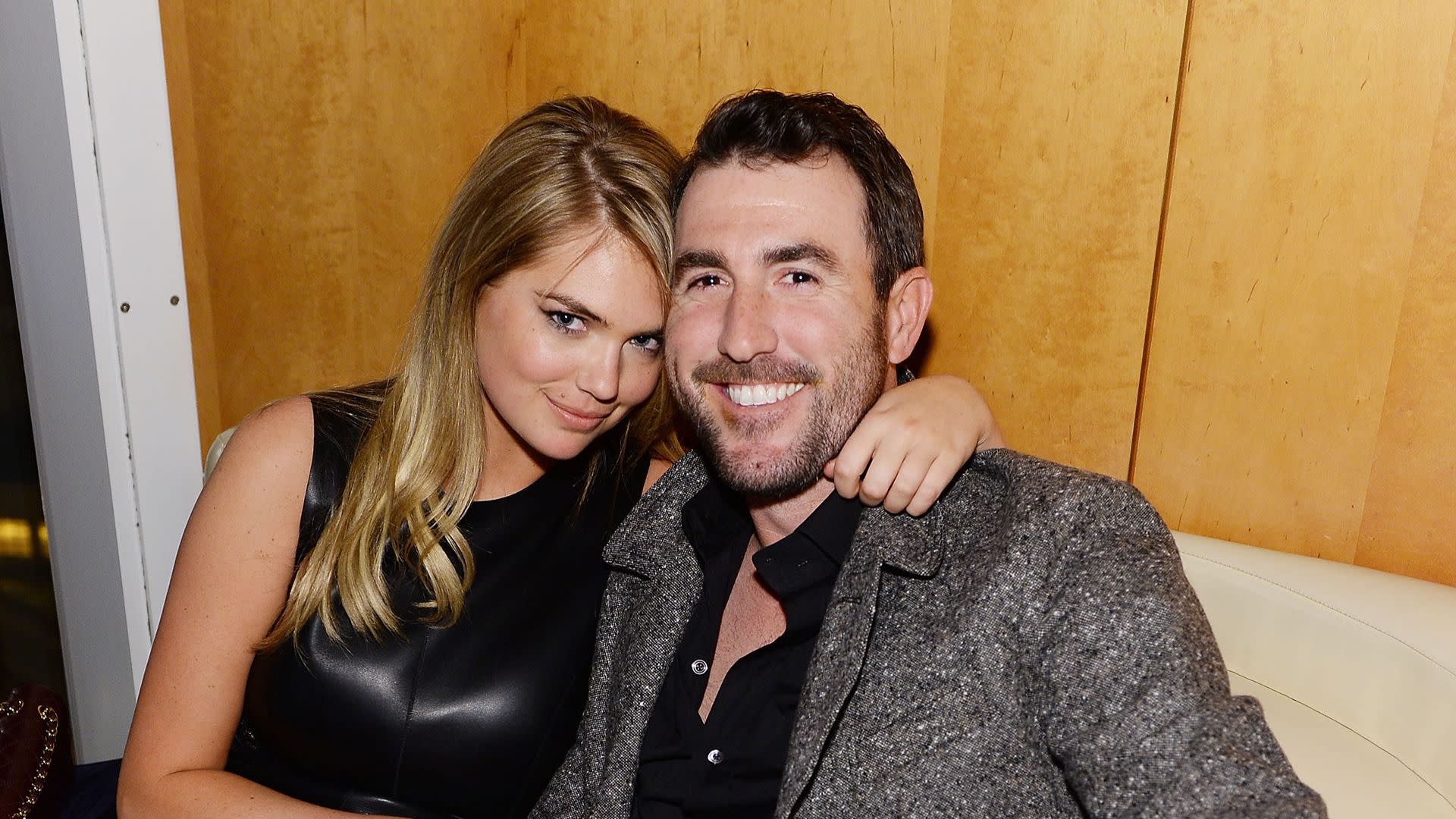 A woman in a black dress and a man in a grey jacket are sitting closely together, smiling at the camera.