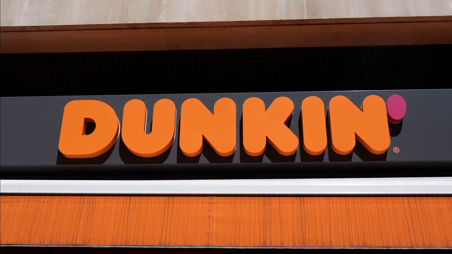The image shows the Dunkin' logo in bold orange letters on a dark background, with a pink apostrophe.