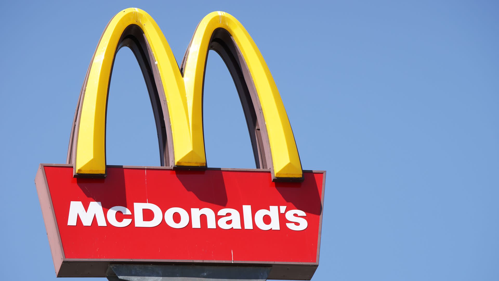 McDonald's sign with the iconic yellow arches on a red background against a clear blue sky.
