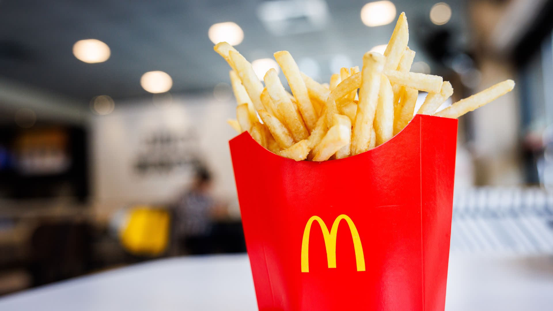 A red McDonald's container filled with French fries on a table in a restaurant setting.