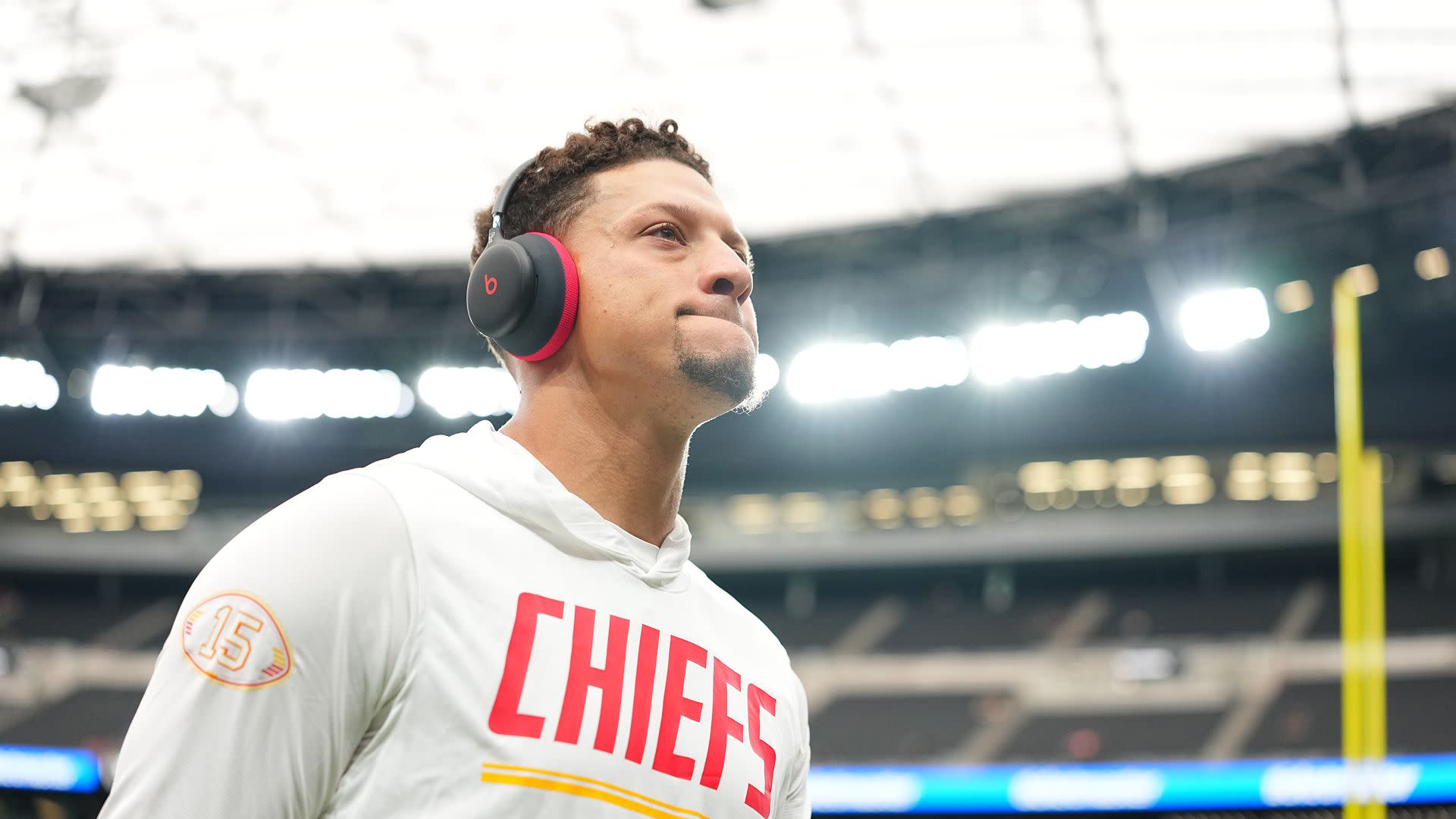 Patrick Mahomes wearing headphones and a Chiefs hoodie, standing in a stadium.