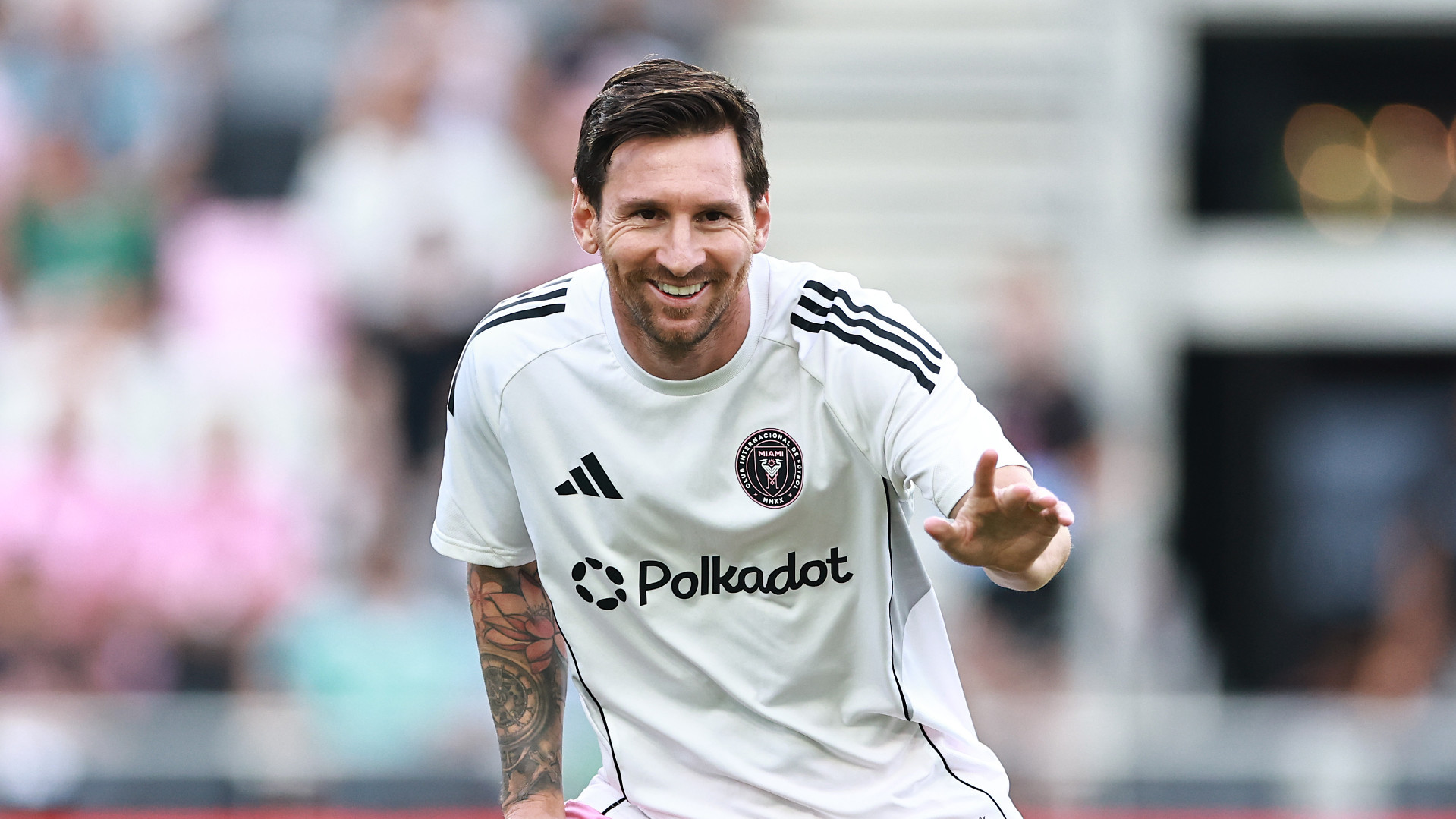Lionel Messi in a white Inter Miami CF jersey, smiling and gesturing on the field.
