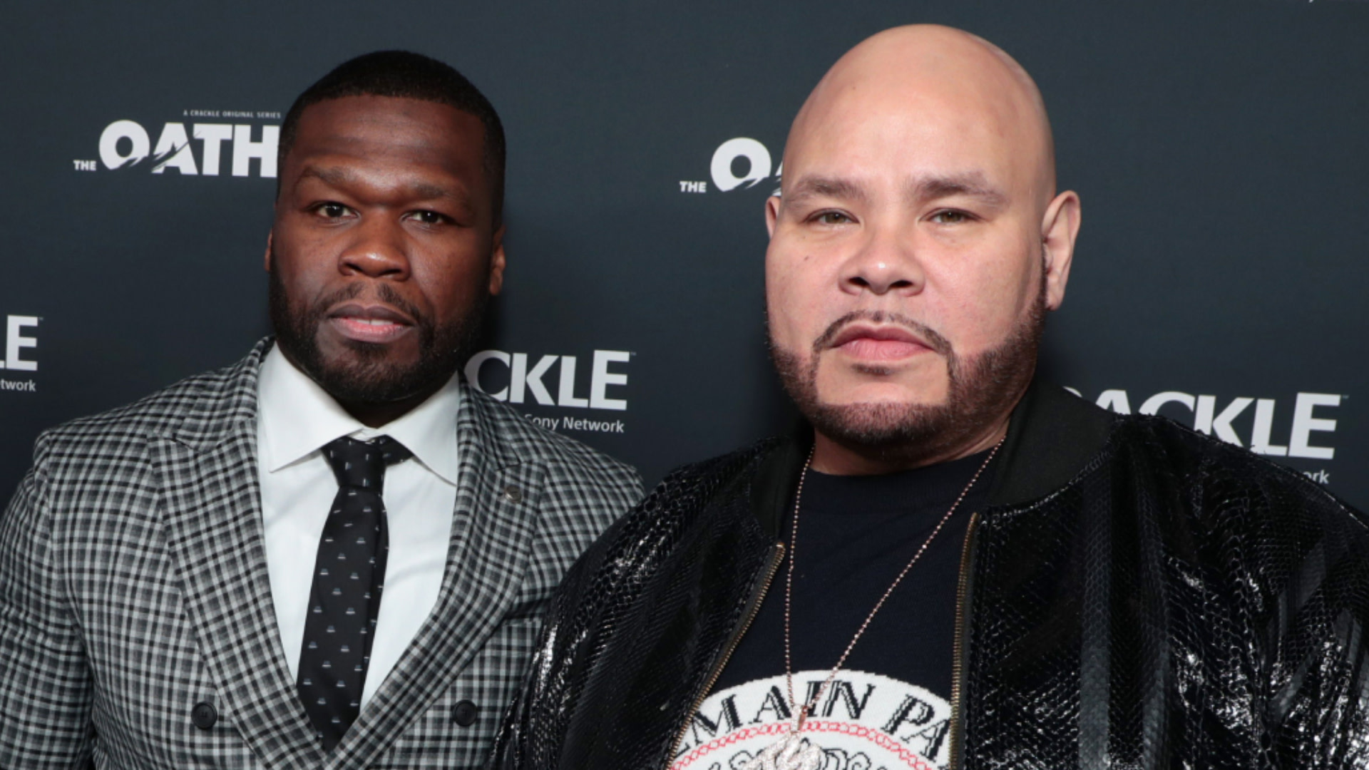 50 Cent in a checkered suit and Fat Joe in a black jacket at an event, posing together.