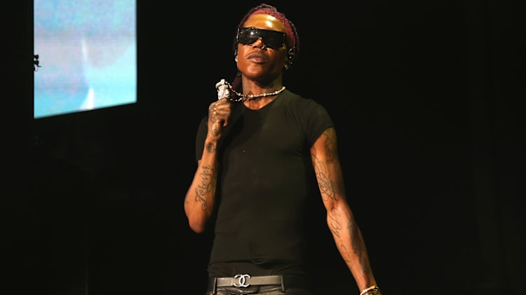 Destroy Lonely wearing sunglasses and a black t-shirt holds a microphone on stage.