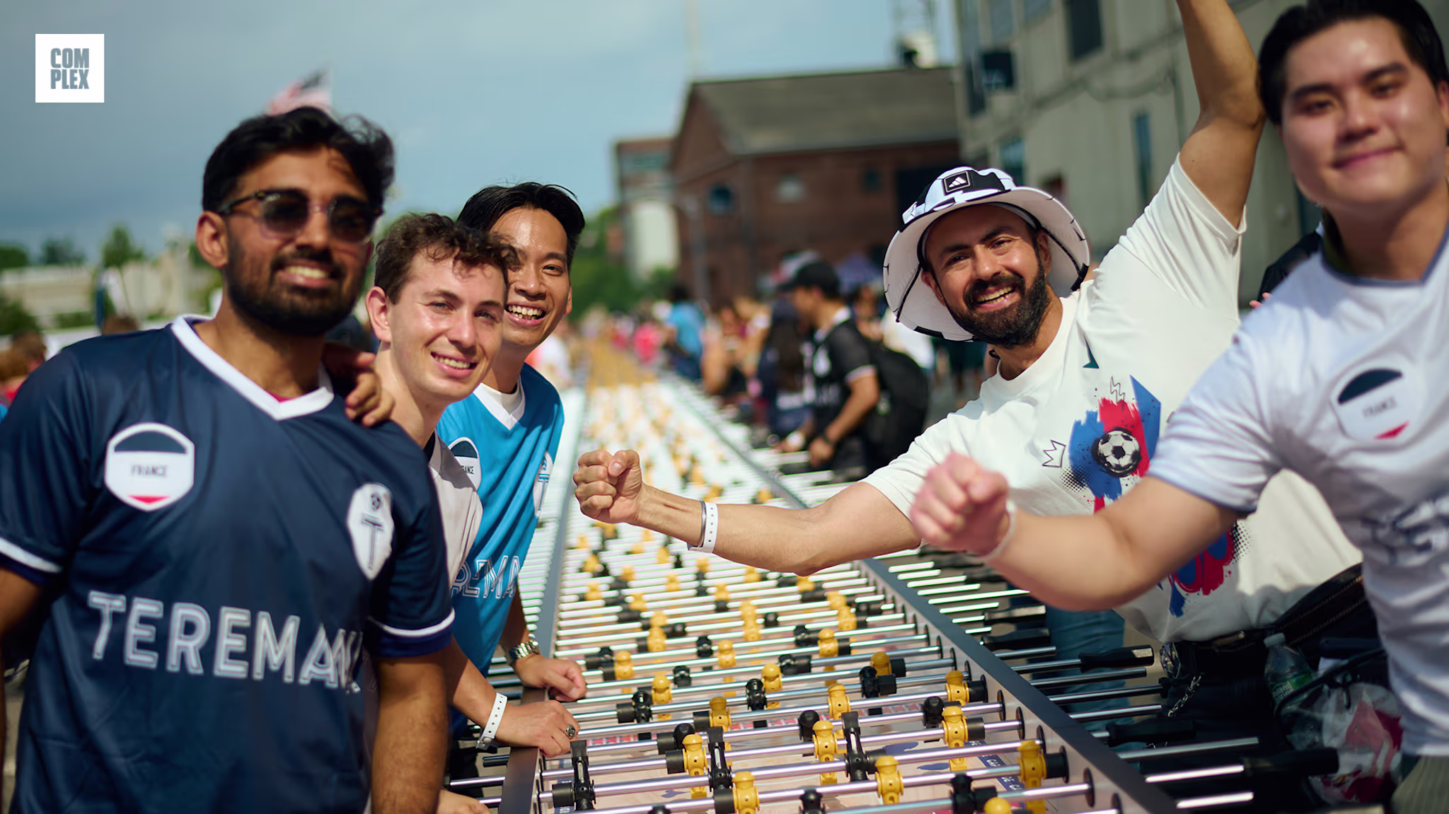 A group of people smiling and posing beside a long foosball table outdoors, with a festive atmosphere.