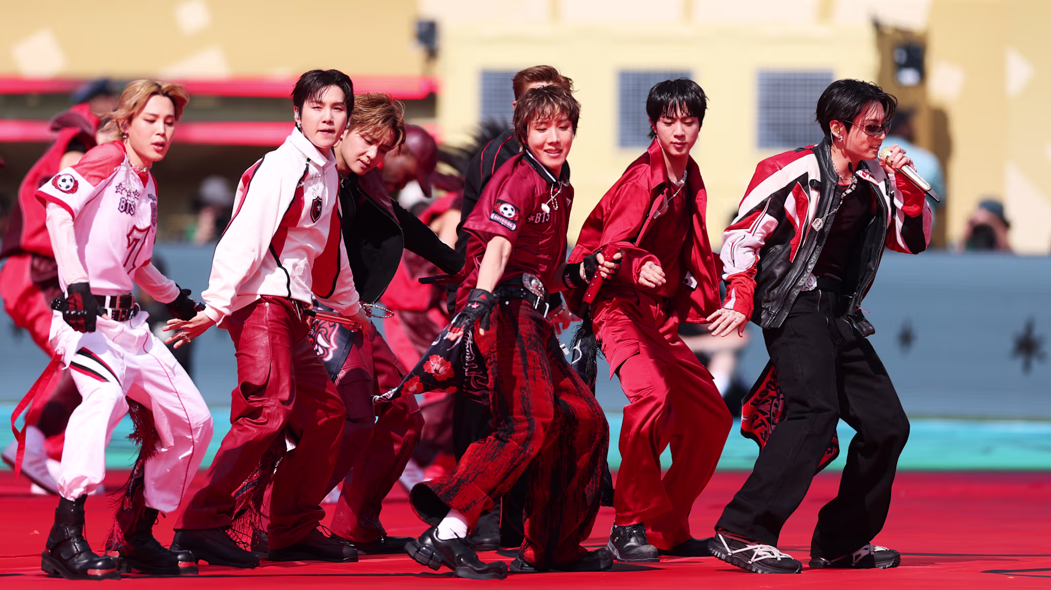 BTS in coordinated red and black outfits dancing energetically on a red stage.