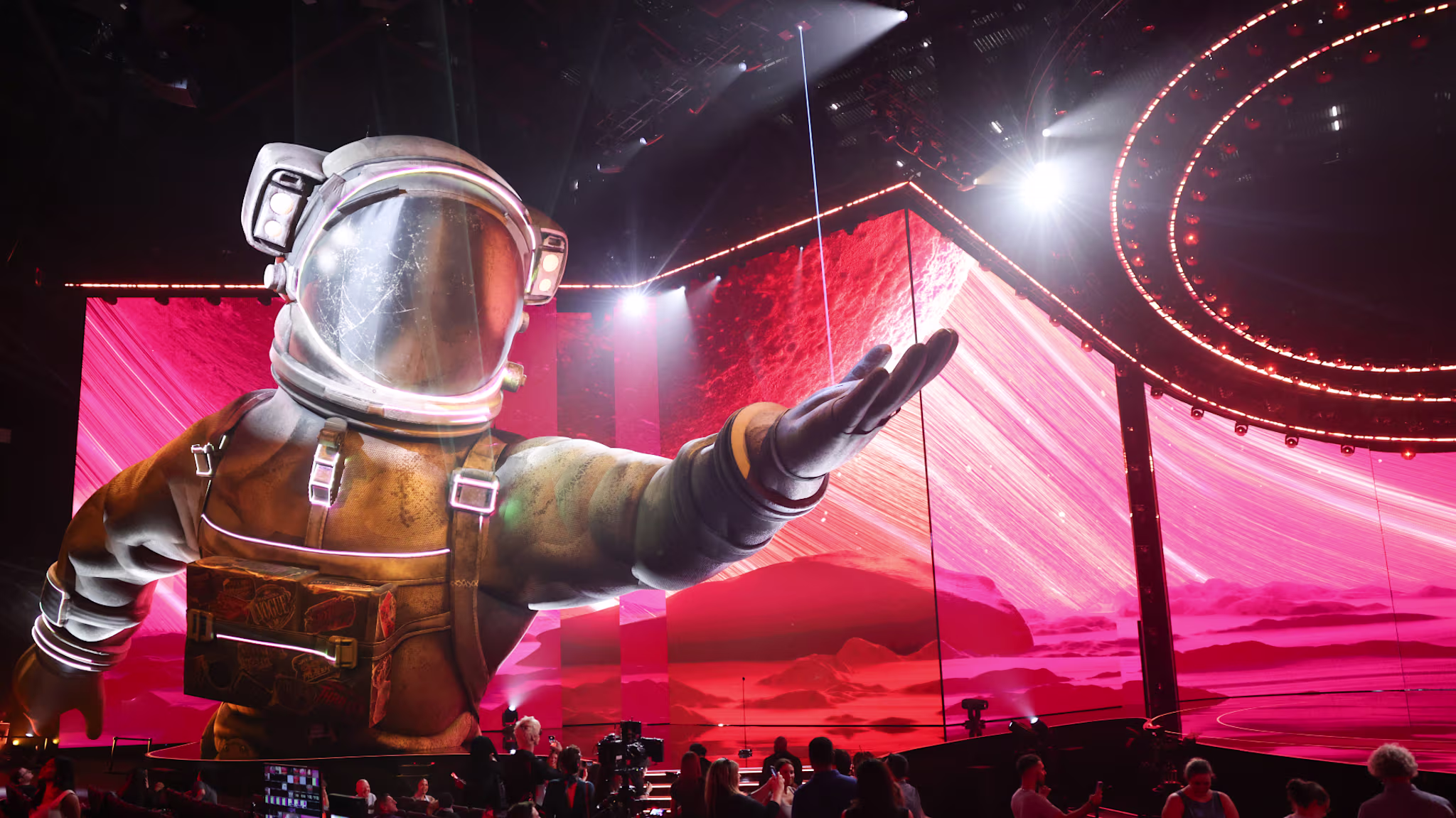 A large astronaut figure on the VMAs stage with vibrant pink and red lighting, surrounded by an audience and circular stage design.