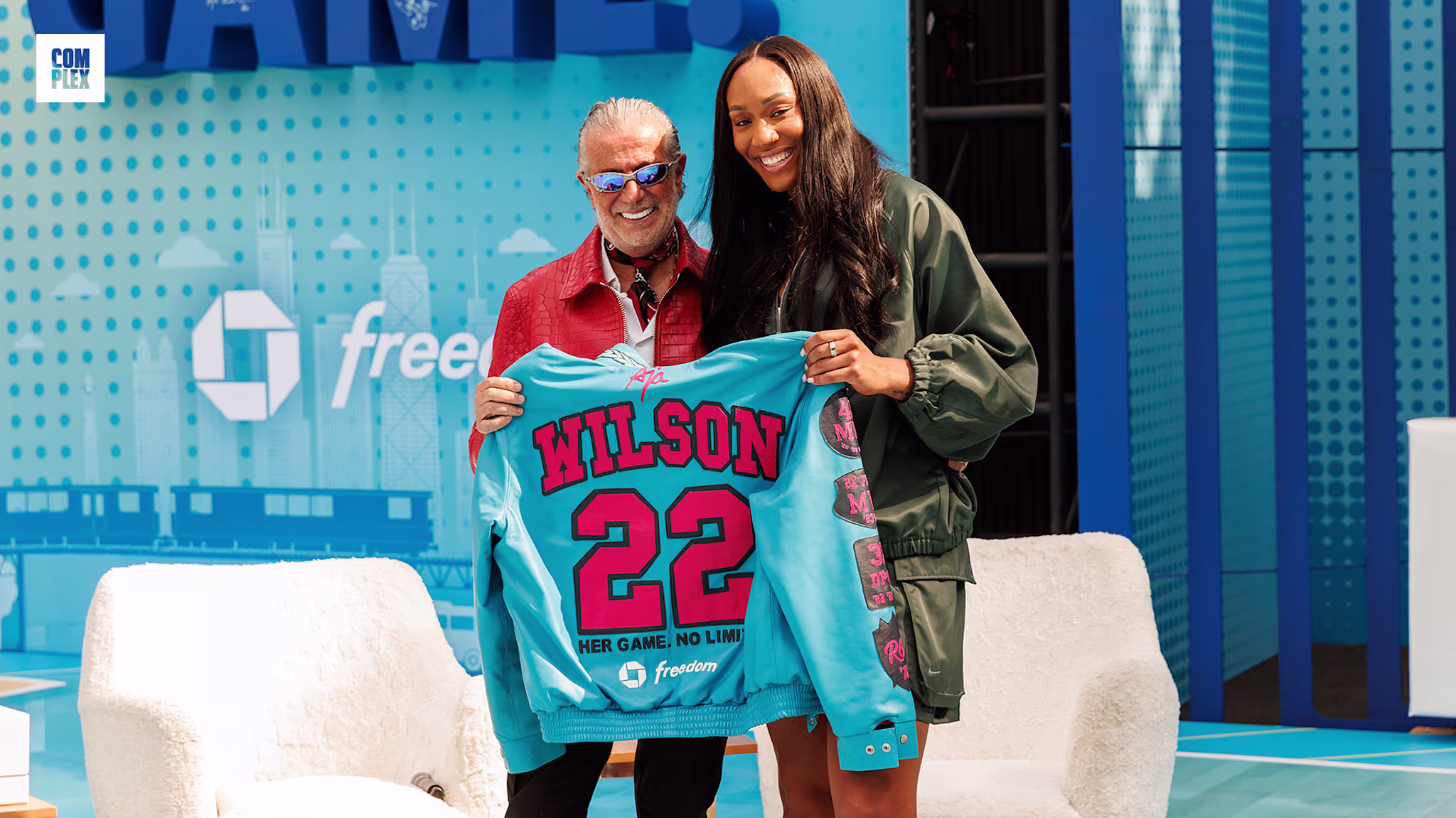 A man and a woman smiling, holding a blue sports jersey with "Wilson 22" printed on it, standing on a stage with blue decor.