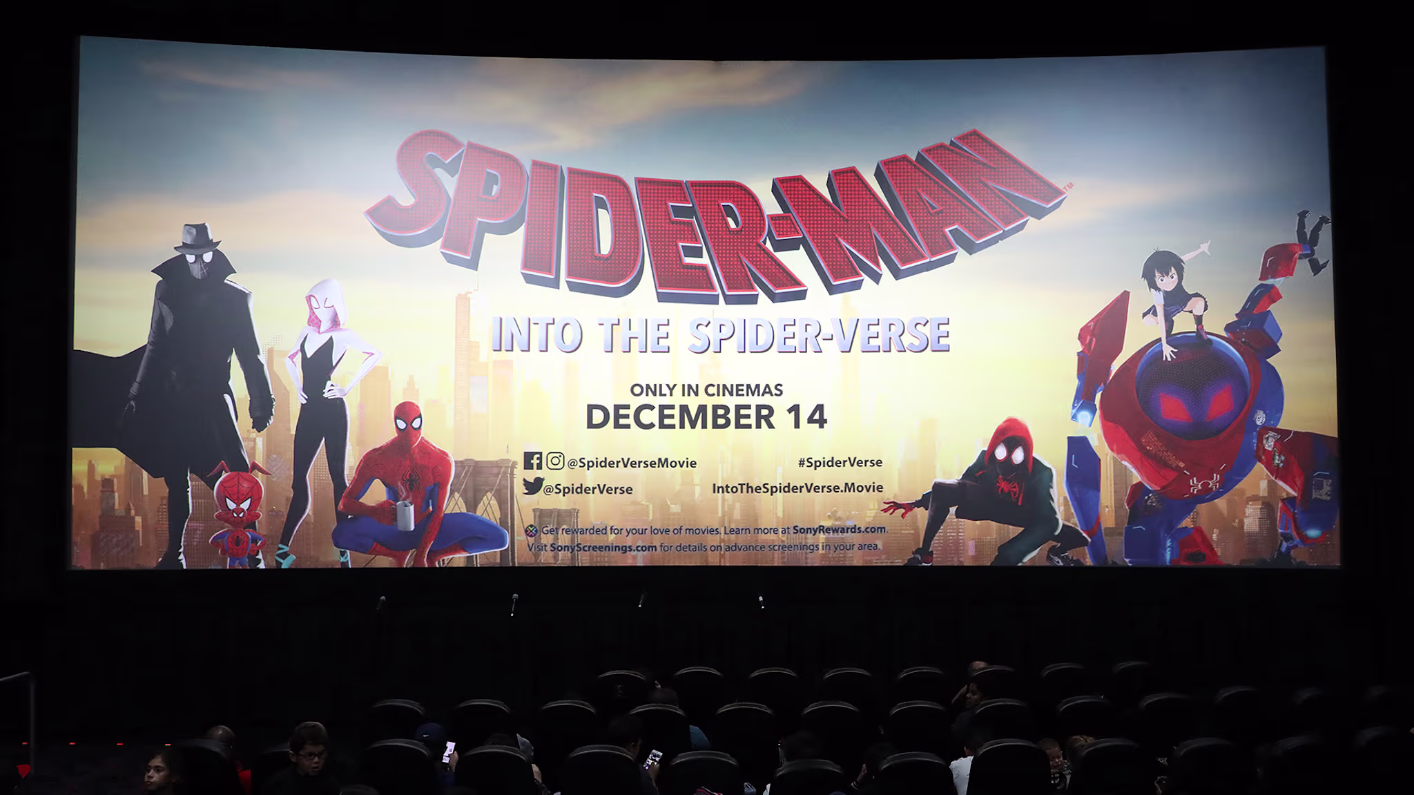 Movie theater screen showing "Spider-Man: Into the Spider-Verse" poster with various Spider-Man characters, release date December 14.