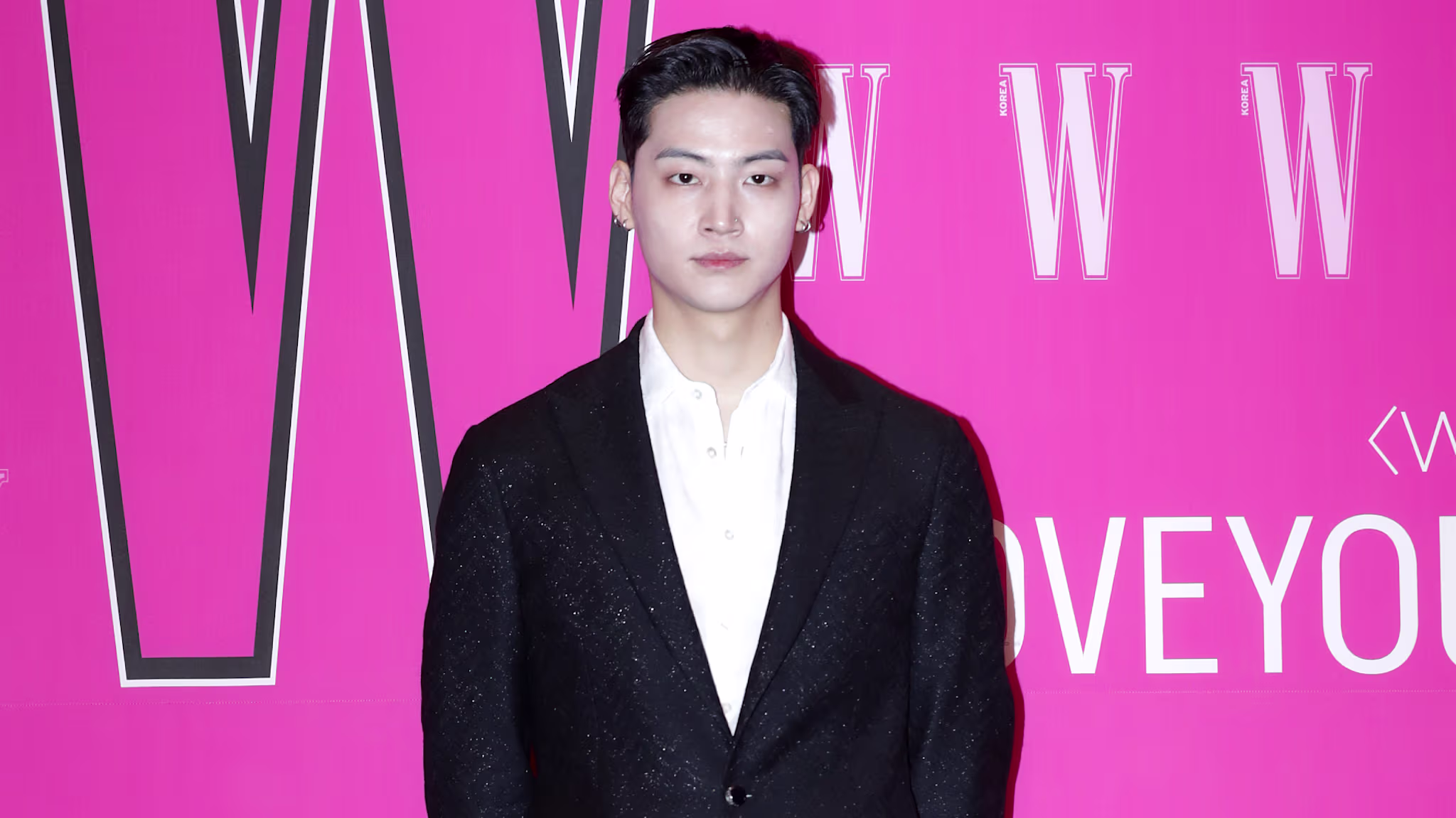 GOT7's Jay B in a black suit stands against a bright pink background with "W" logos.