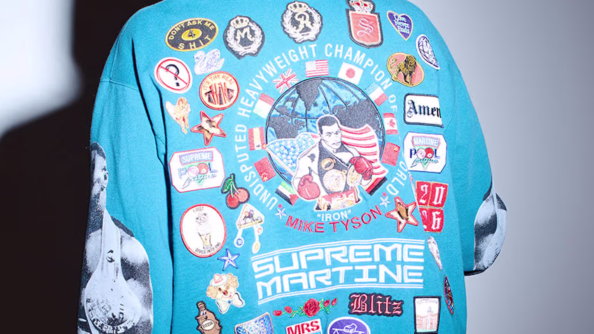 A blue hoodie with various colorful patches and graphics, including a prominent illustration of boxer Mike Tyson and the text "Supreme Martine."