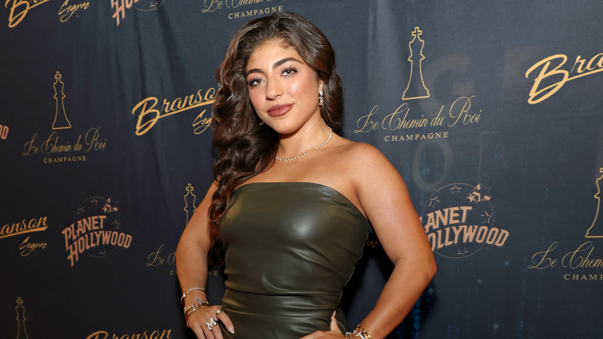 A woman in a strapless dark dress poses in front of a branded backdrop, featuring logos like Planet Hollywood and Branson Cognac.