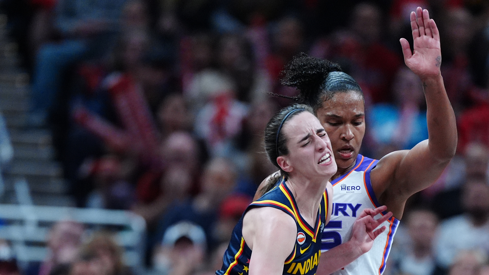 Two female basketball players in action during a game. One is wearing a yellow and blue jersey, the other a white and purple jersey.