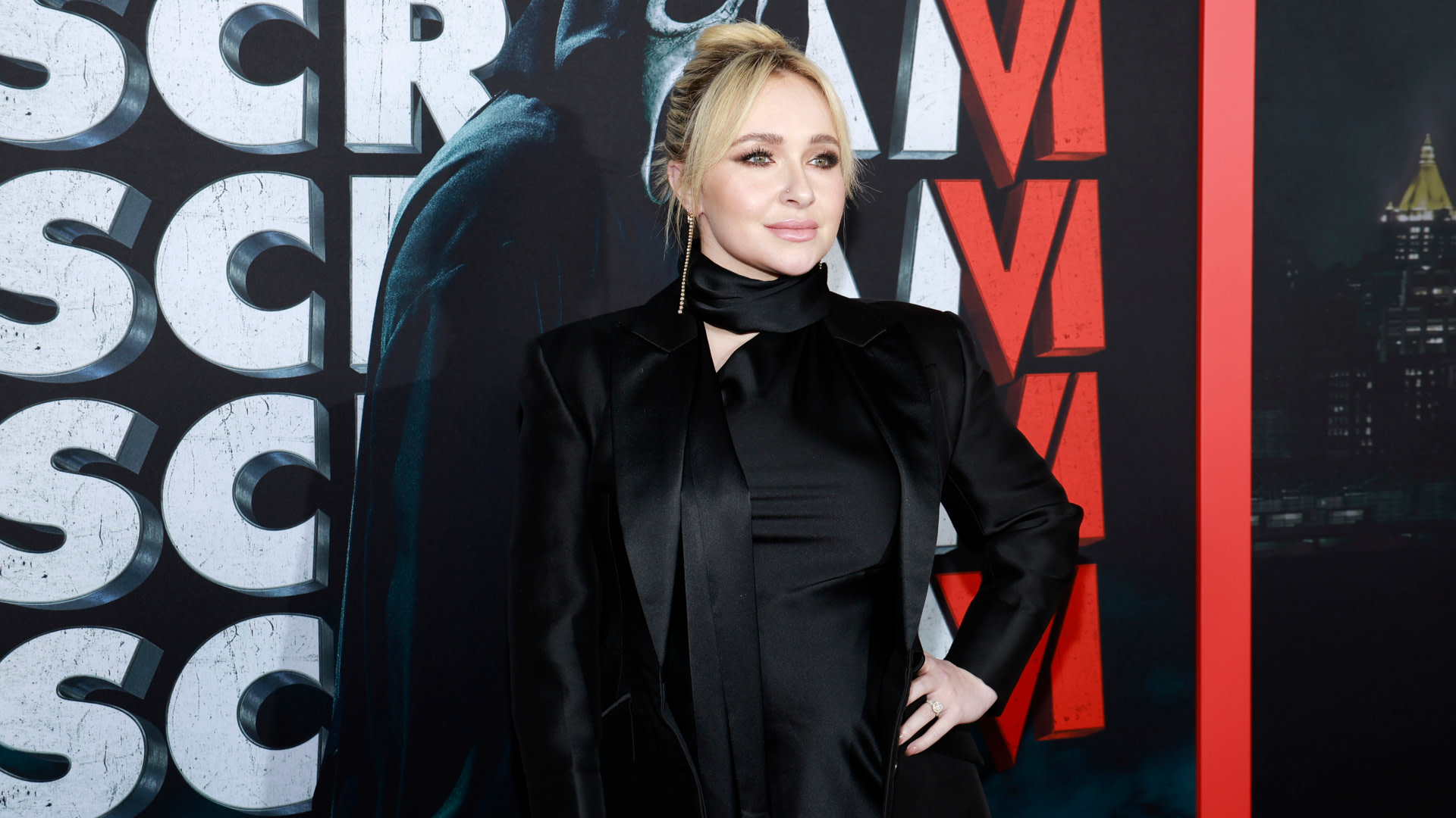 Hayden Panettiere at the "Scream VI" premiere, wearing a black outfit, standing in front of the movie poster.