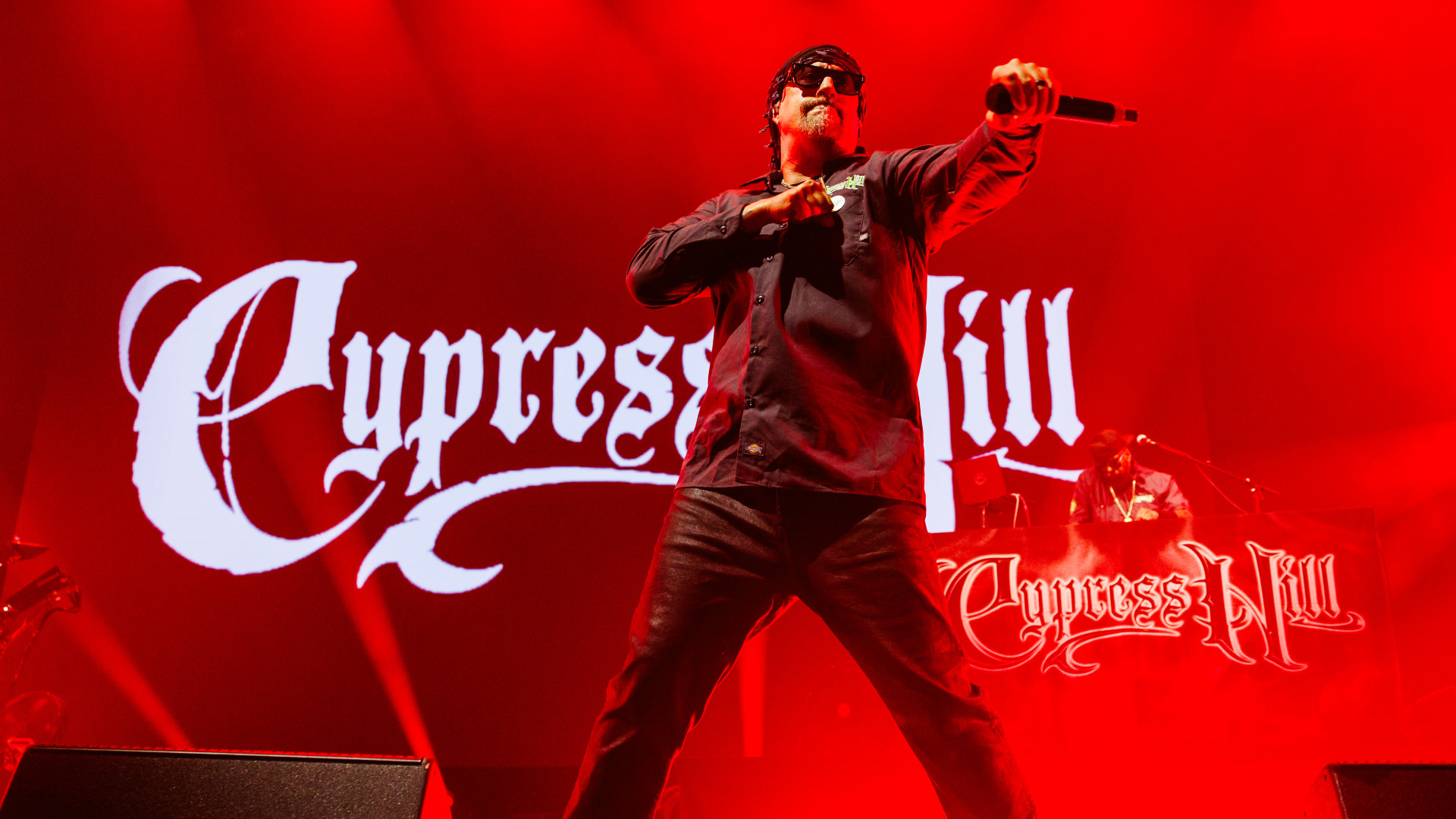 Cypress Hill performing on stage with vibrant red lighting, their logo displayed prominently in the background.