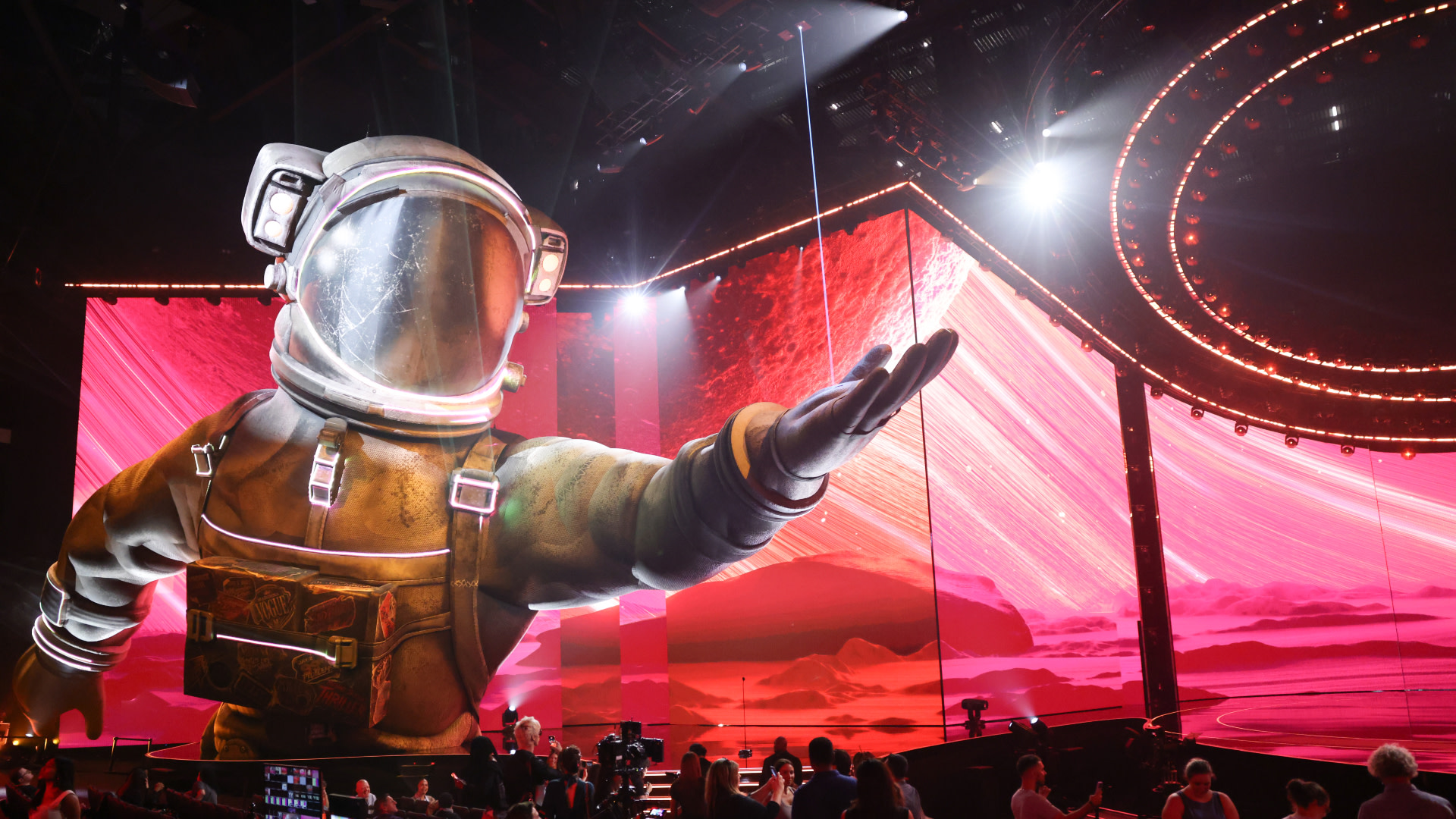 A large astronaut figure on the VMAs stage with vibrant pink and red lighting, surrounded by an audience and circular stage design.