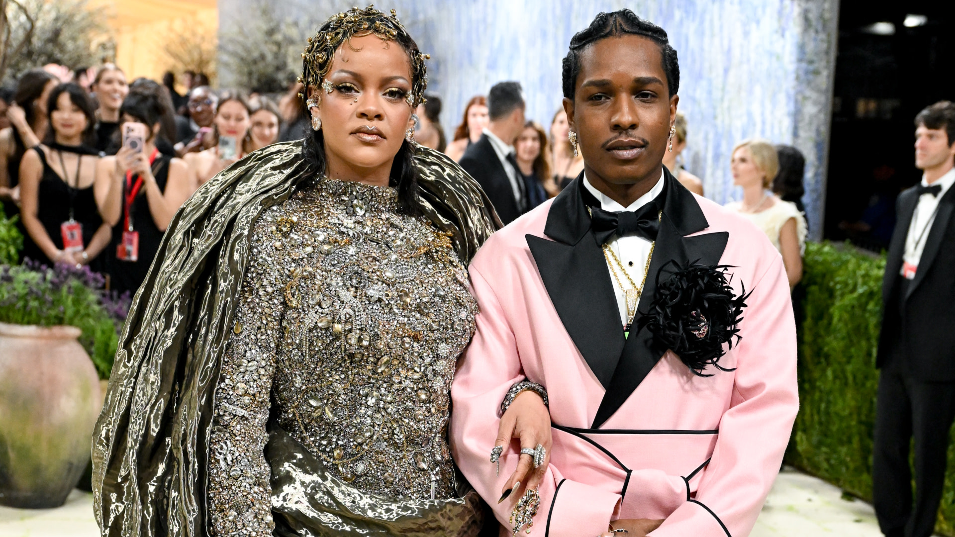 Rihanna and A$AP Rocky at a formal event. Rihanna wears an ornate gown with a headpiece, and A$AP Rocky dons a pink tuxedo.