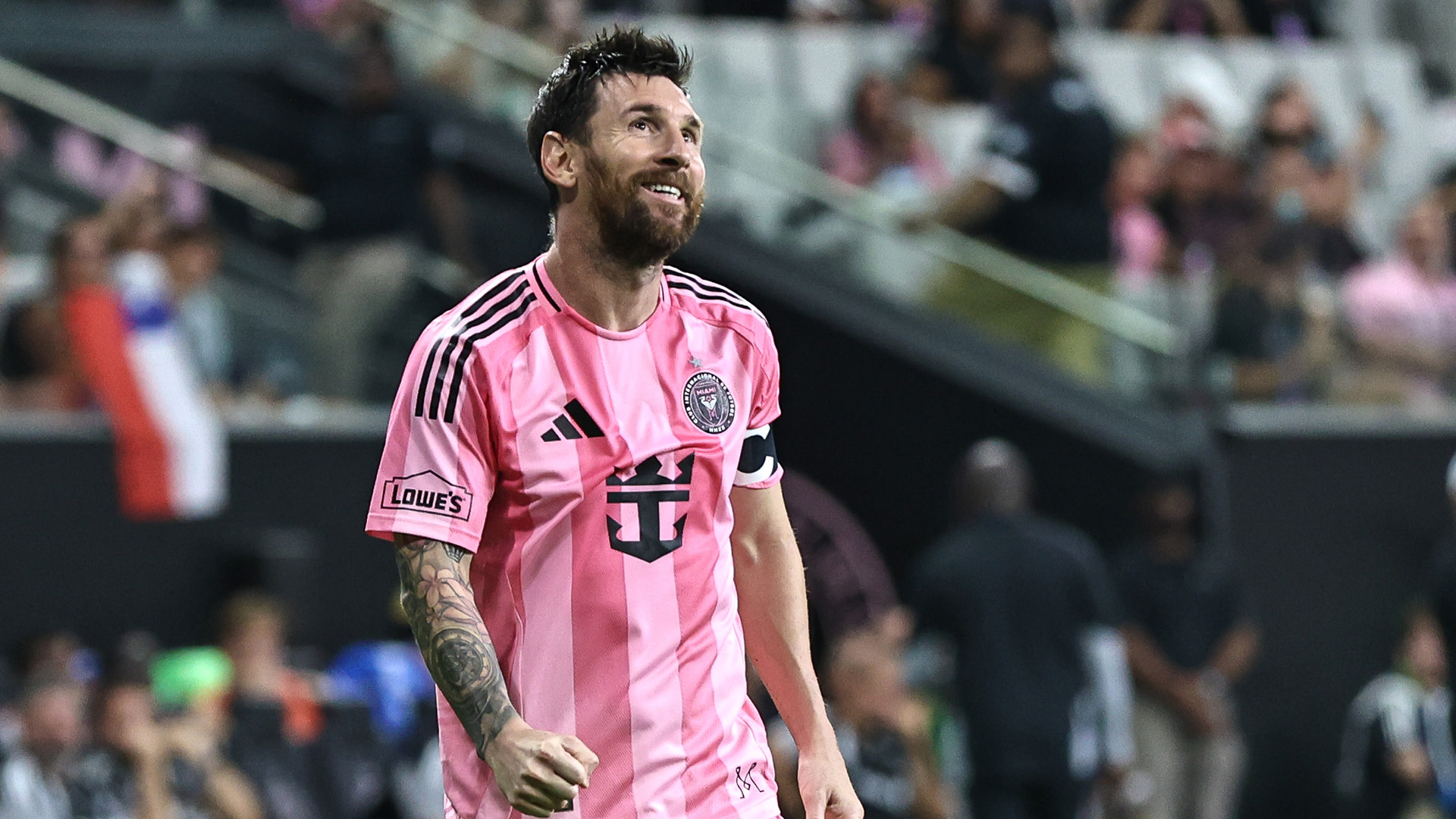 Lionel Messi in a pink Inter Miami CF jersey, smiling on a soccer field during a match.
