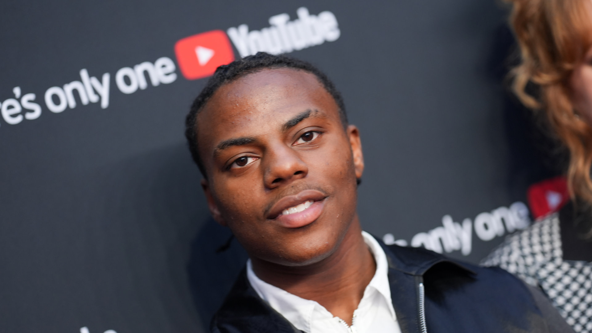 Speed smiling at an event with a YouTube backdrop.