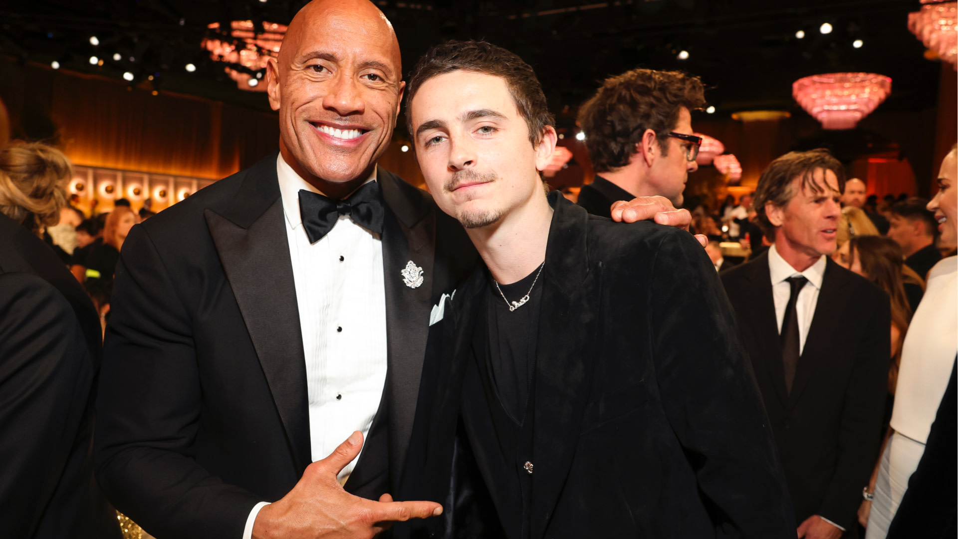 Dwayne "The Rock" Johnson in a tuxedo, smiling with Timothée Chalamet in a black suit at a formal event.