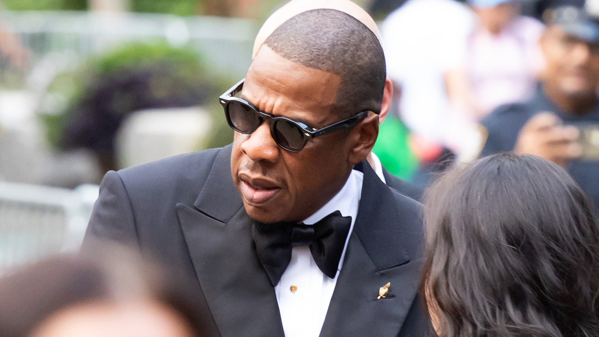 Jay-Z in a tuxedo and sunglasses at an outdoor event.