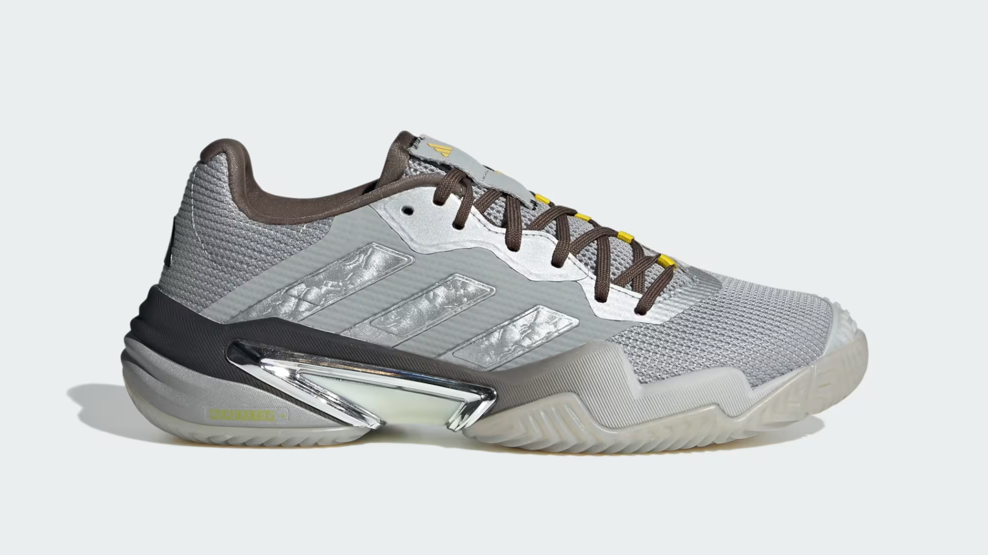 A gray Adidas sneaker with a textured mesh upper, brown laces, and metallic silver accents on the side and heel.