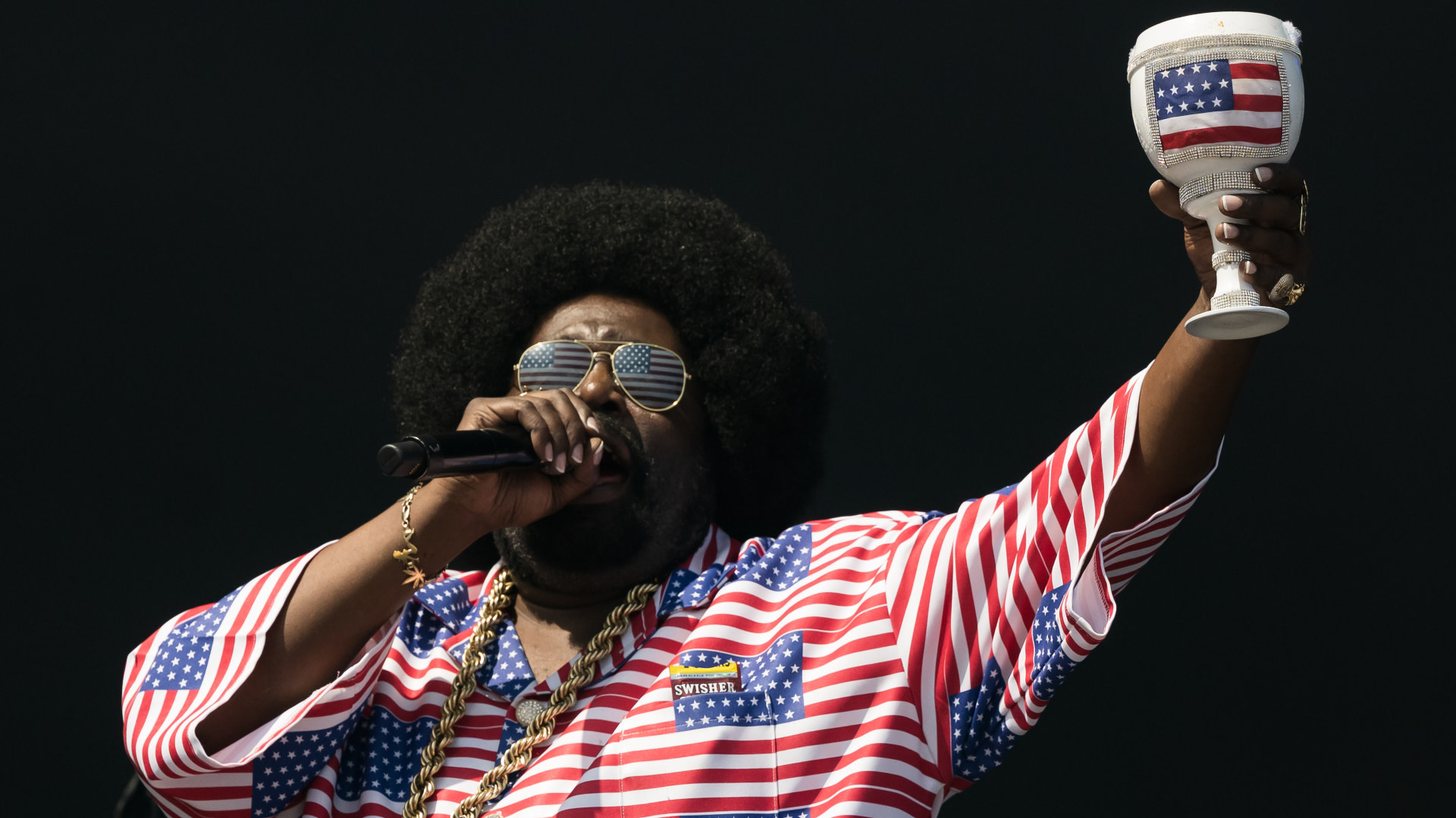 Afroman performing, wearing a red, white, and blue stars and stripes outfit, holding a goblet with a matching design, and sunglasses.
