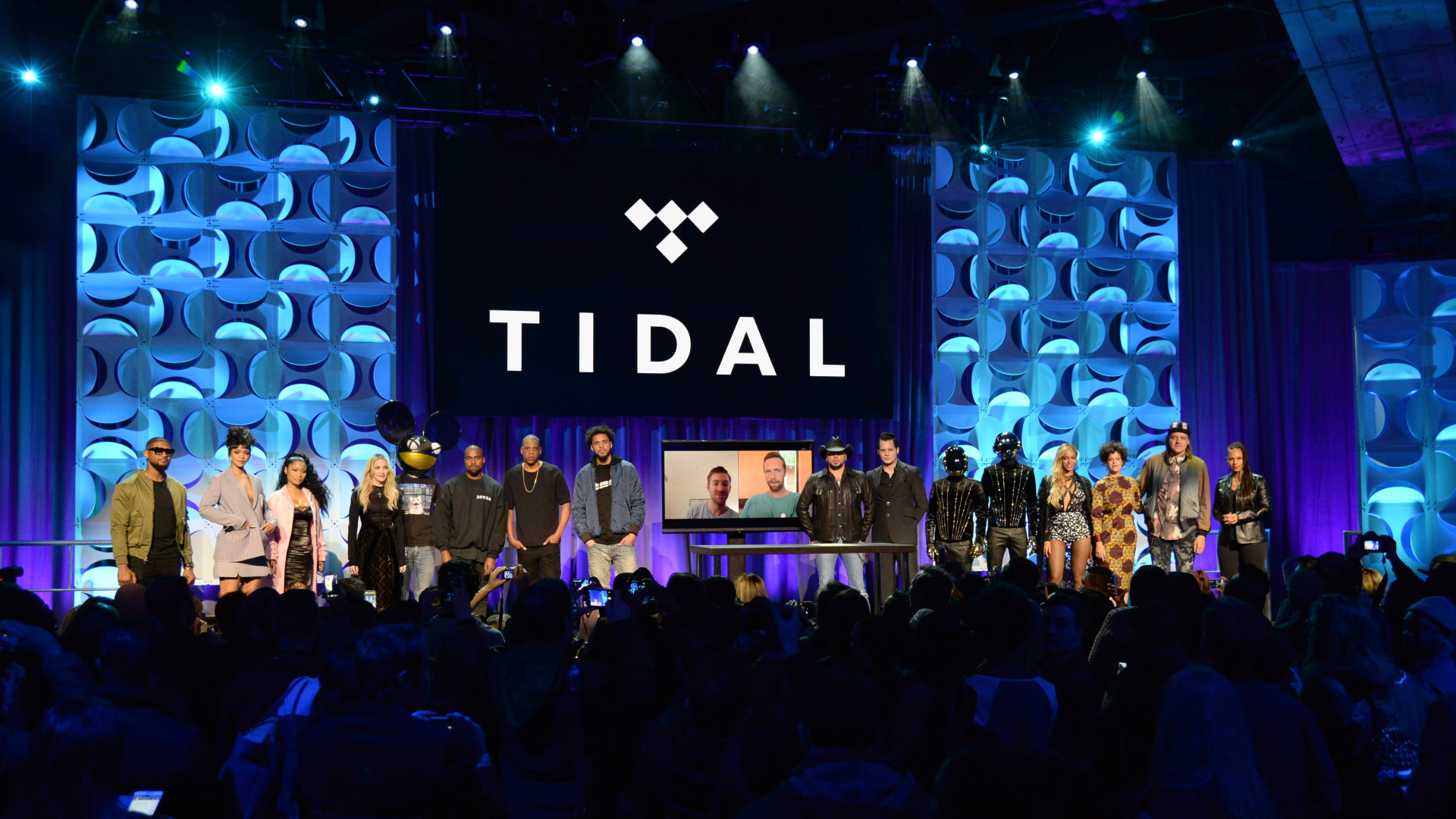 A group of celebrities, including Jay-Z, Madonna, and Daft Punk, on stage at a Tidal event with a blue-lit backdrop.