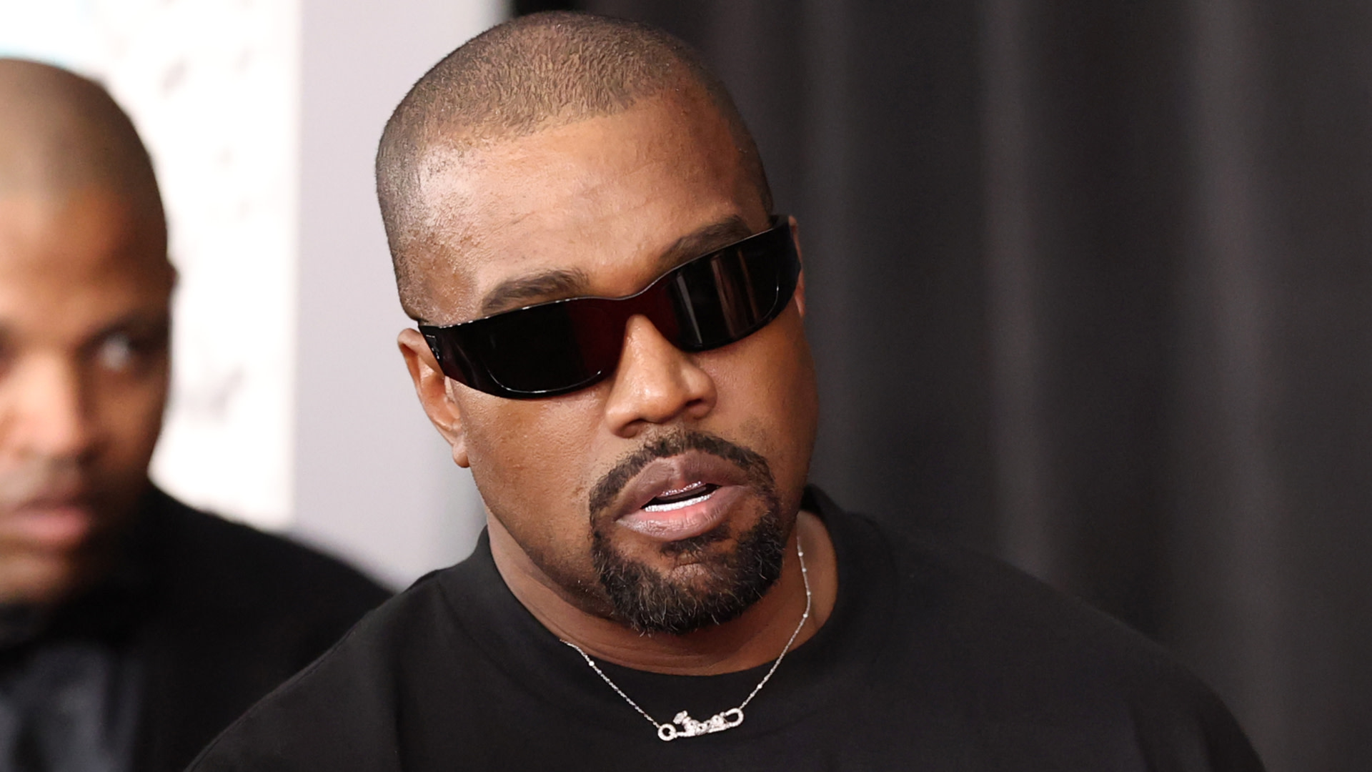 Kanye West wearing sunglasses and a black shirt at an event.