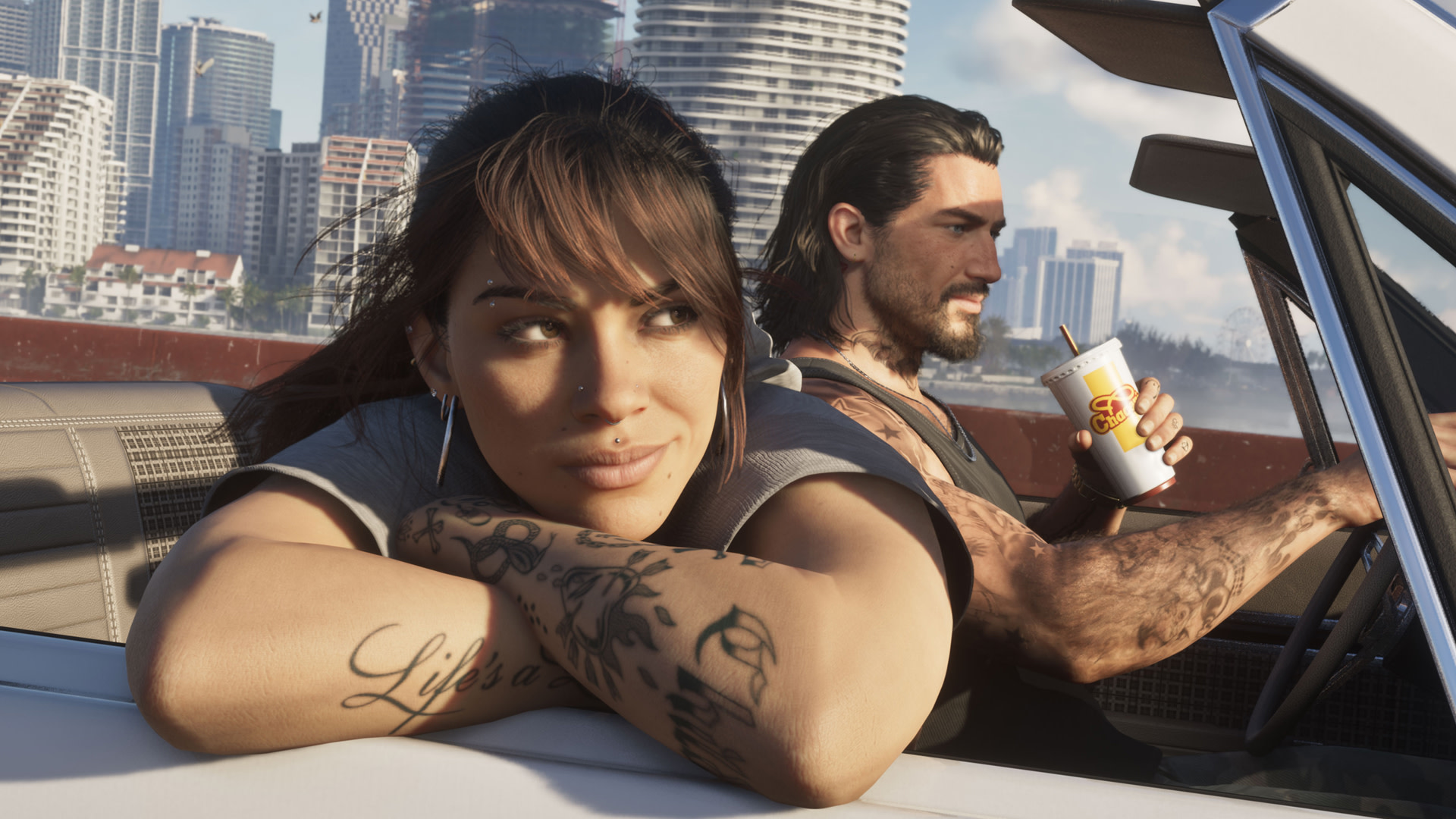 A woman with tattoos leans on a car door, smiling. A man with long hair and tattoos drives, holding a drink. City skyline in the background.