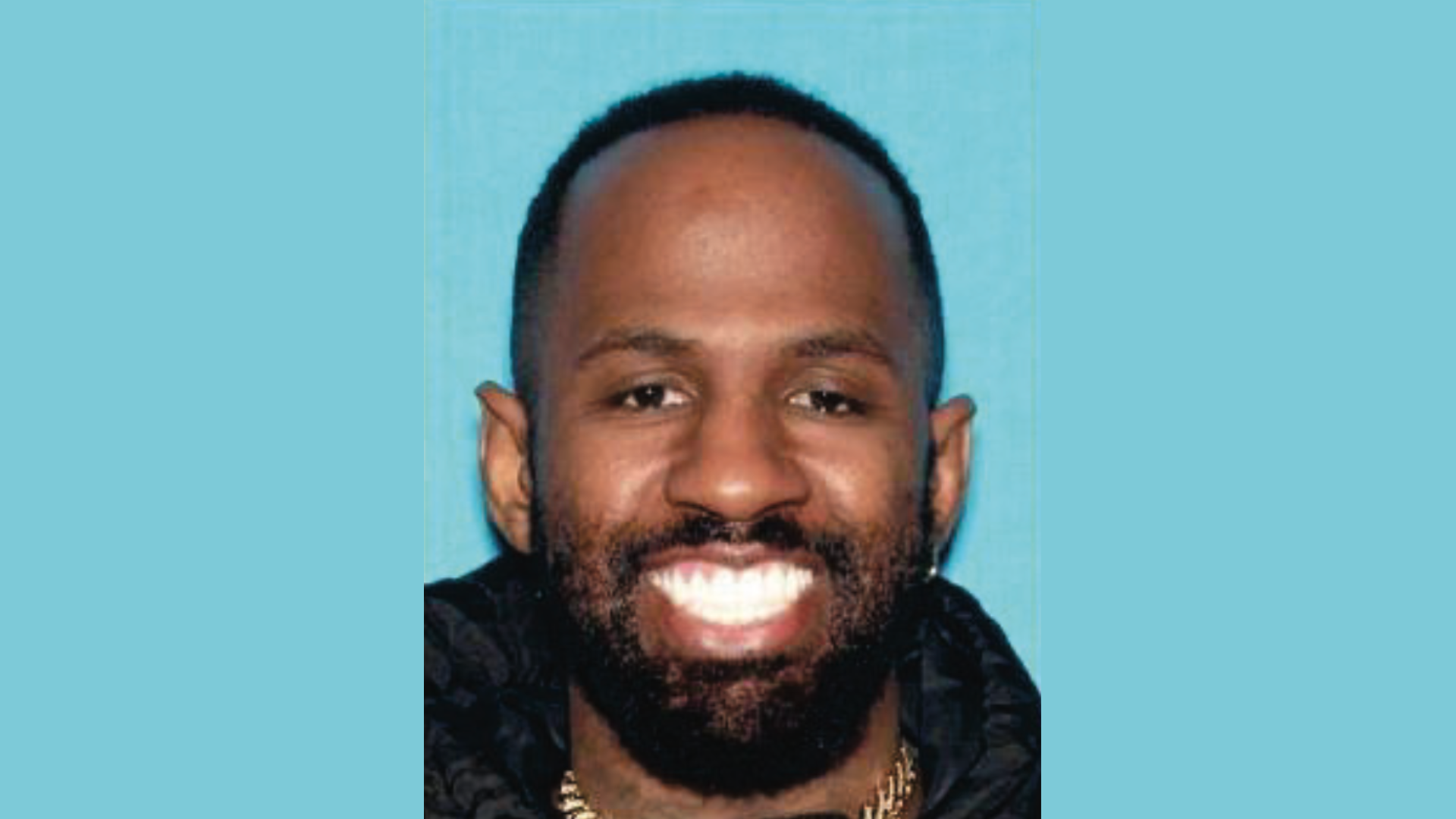 Daejon Love with a beard smiles against a solid blue background.