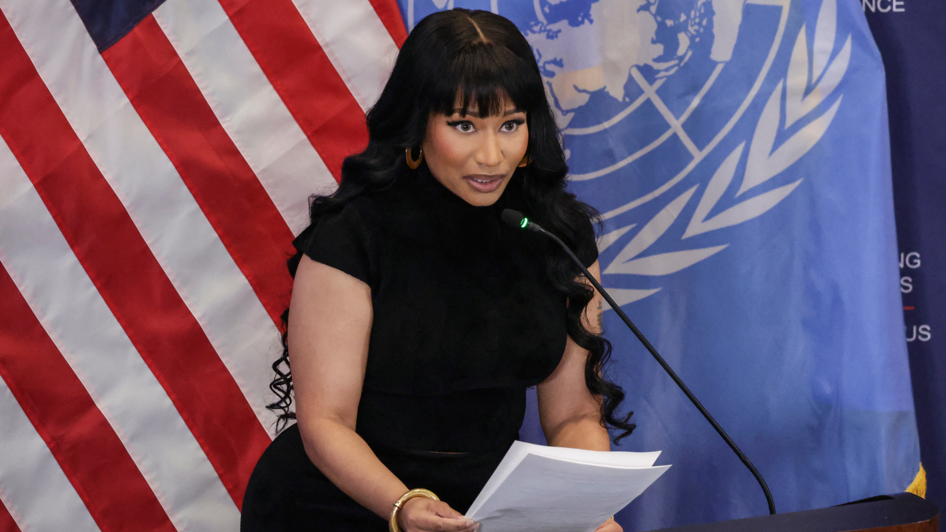 Nicki Minaj speaking at a podium with an American flag and UN flag in the background.