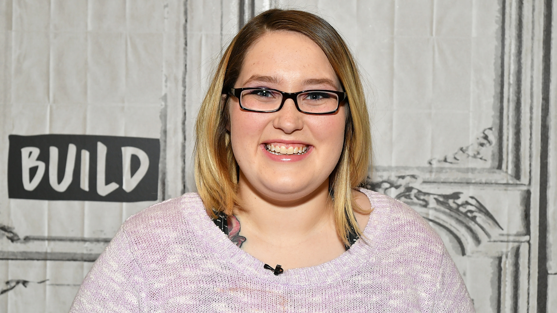 Lauryn "Pumpkin" Efird, circa 2019, with glasses and a light purple sweater smiles in front of a backdrop.