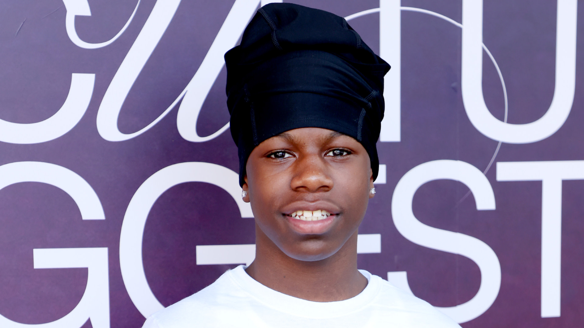RaKai wearing a black headwrap and a white shirt, smiling in front of a purple background with white text.
