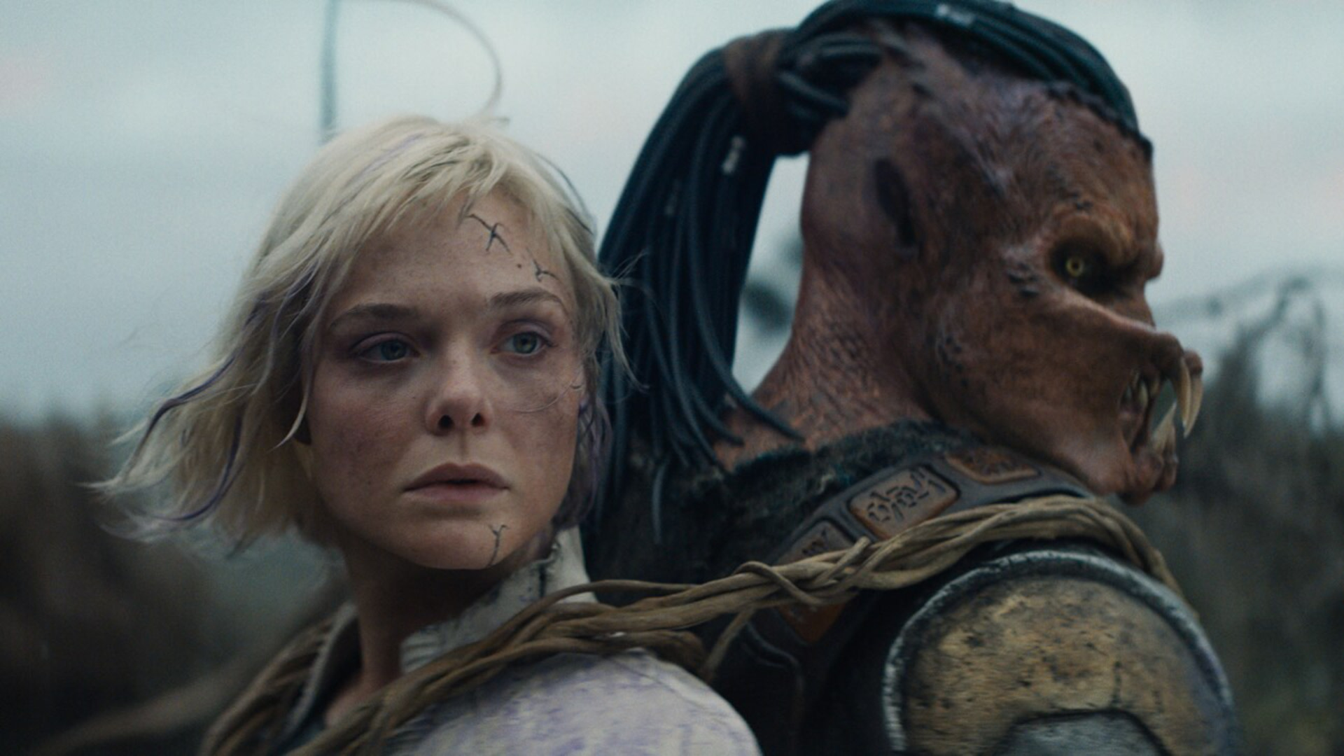 A woman with short blonde hair and facial markings stands beside a creature with a reptilian appearance and dreadlocks.