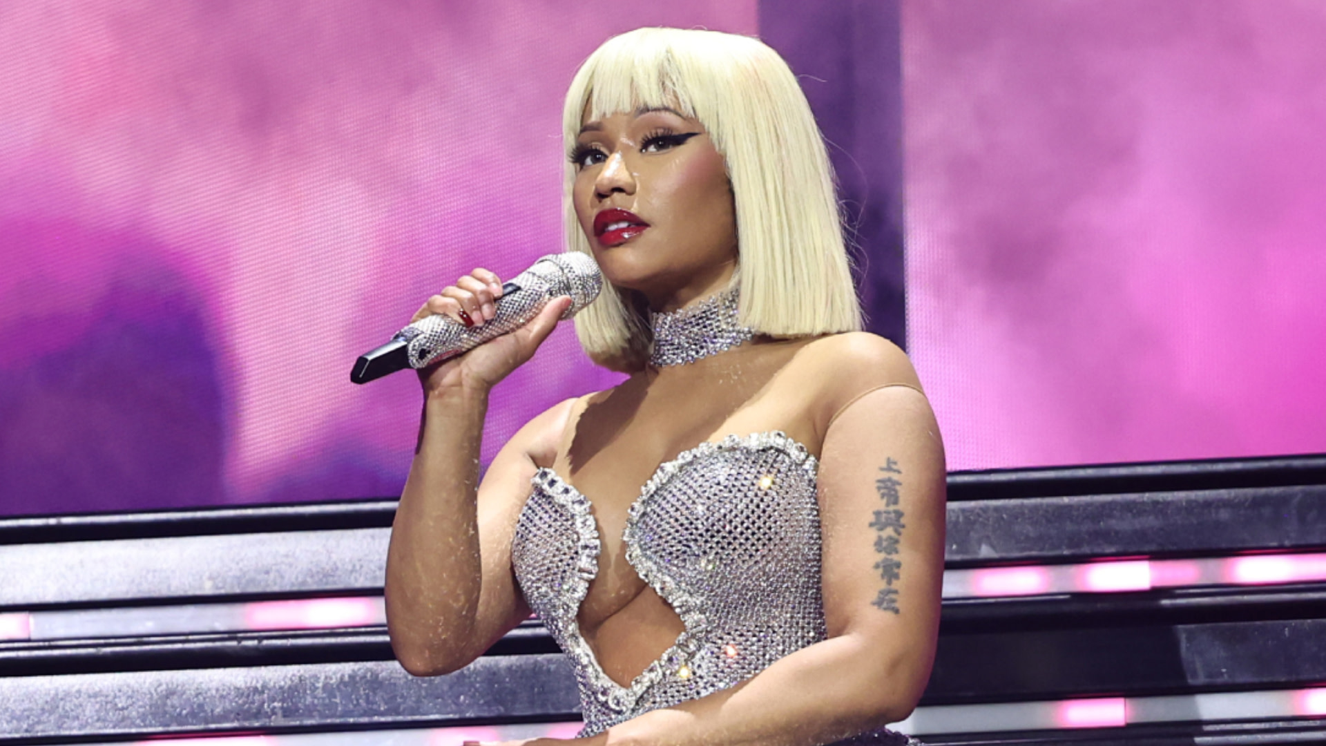 Nicki Minaj performing on stage in a sparkling silver outfit, holding a microphone.
