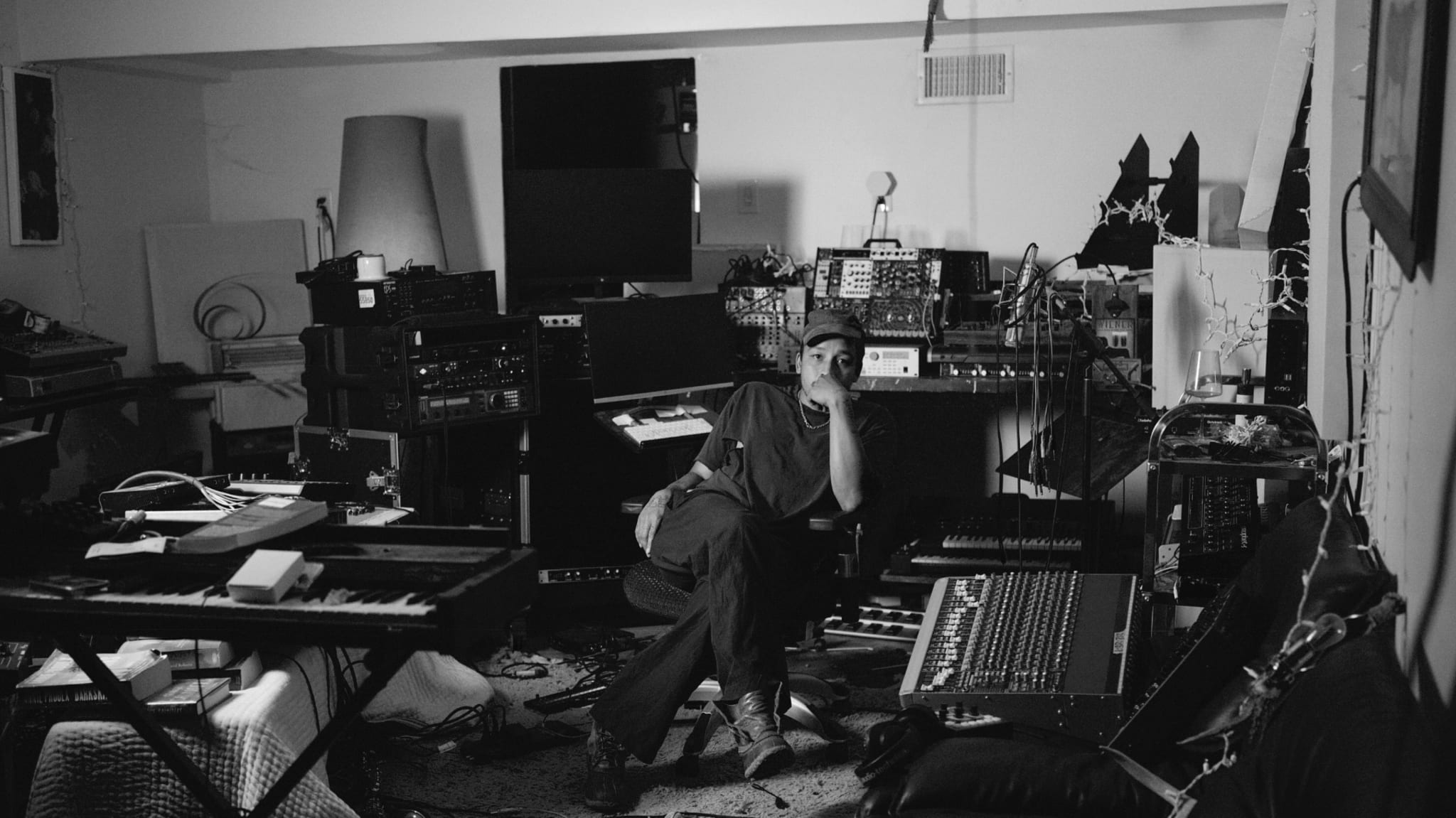 Dijon sits in a dimly lit recording studio surrounded by keyboards, mixing consoles, and electronic equipment.