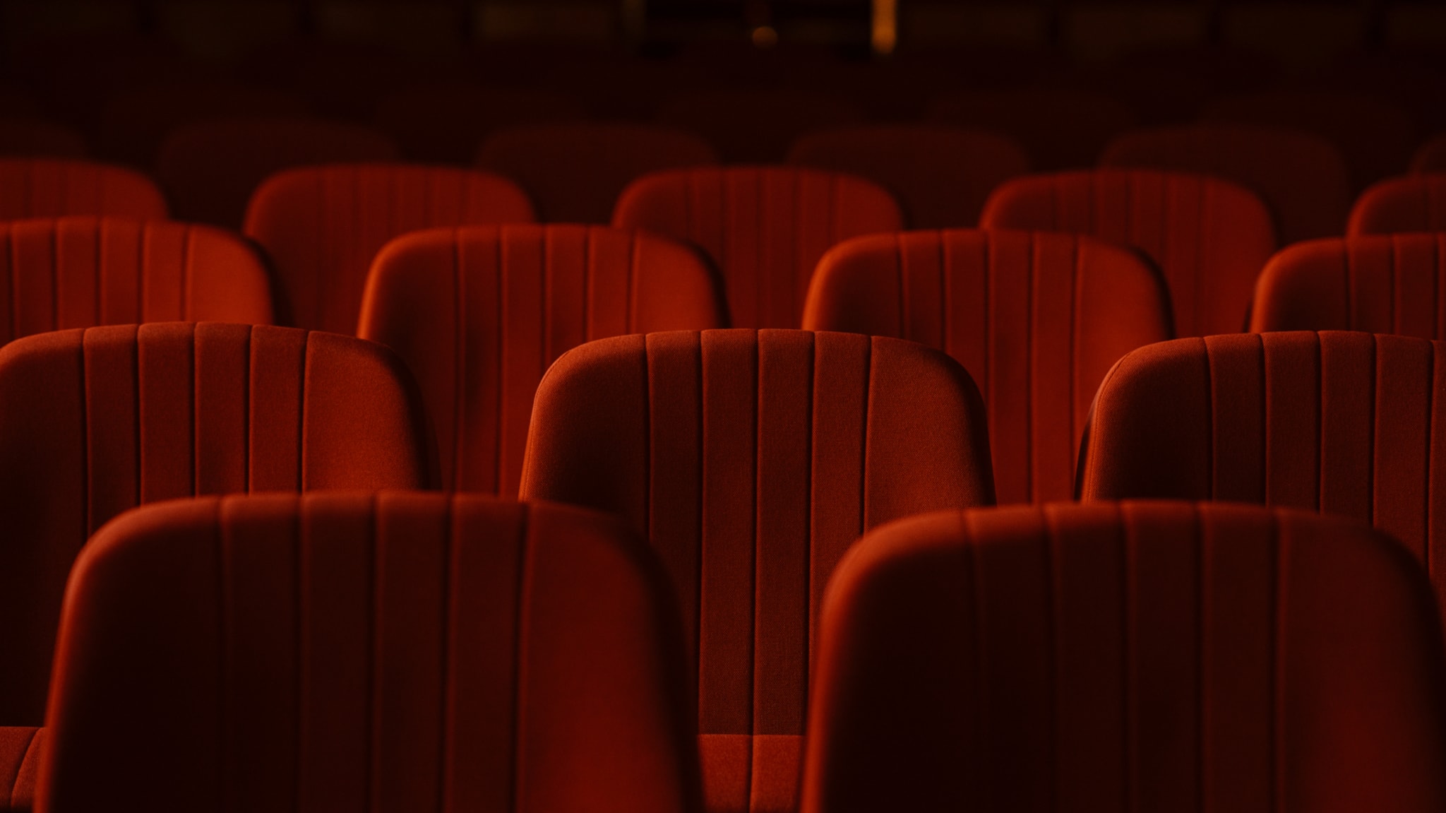 Empty red theater seats arranged in rows, dimly lit, creating a warm and inviting atmosphere.