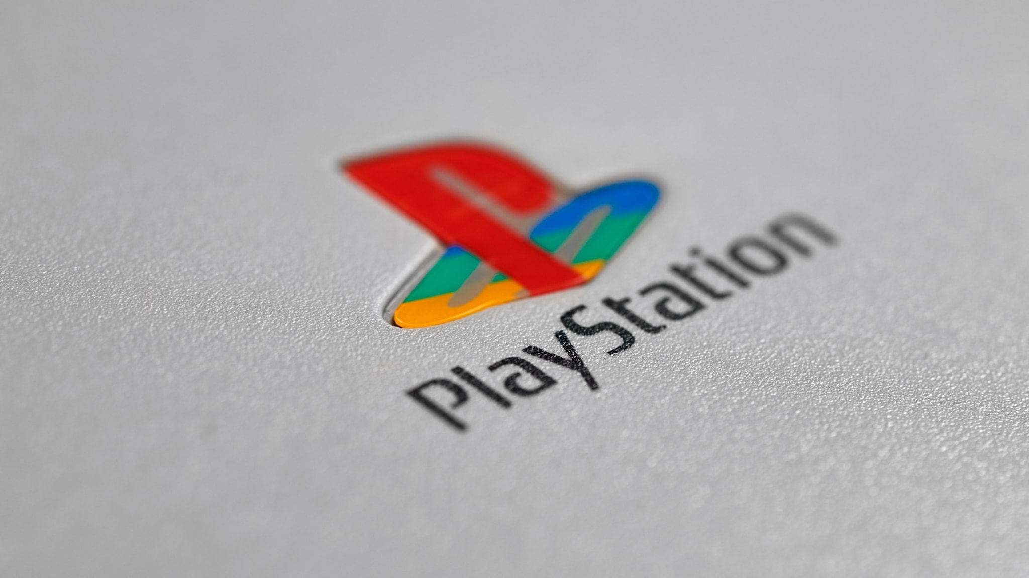 Close-up of the PlayStation logo on a gray surface, featuring a colorful "PS" symbol above the word "PlayStation."