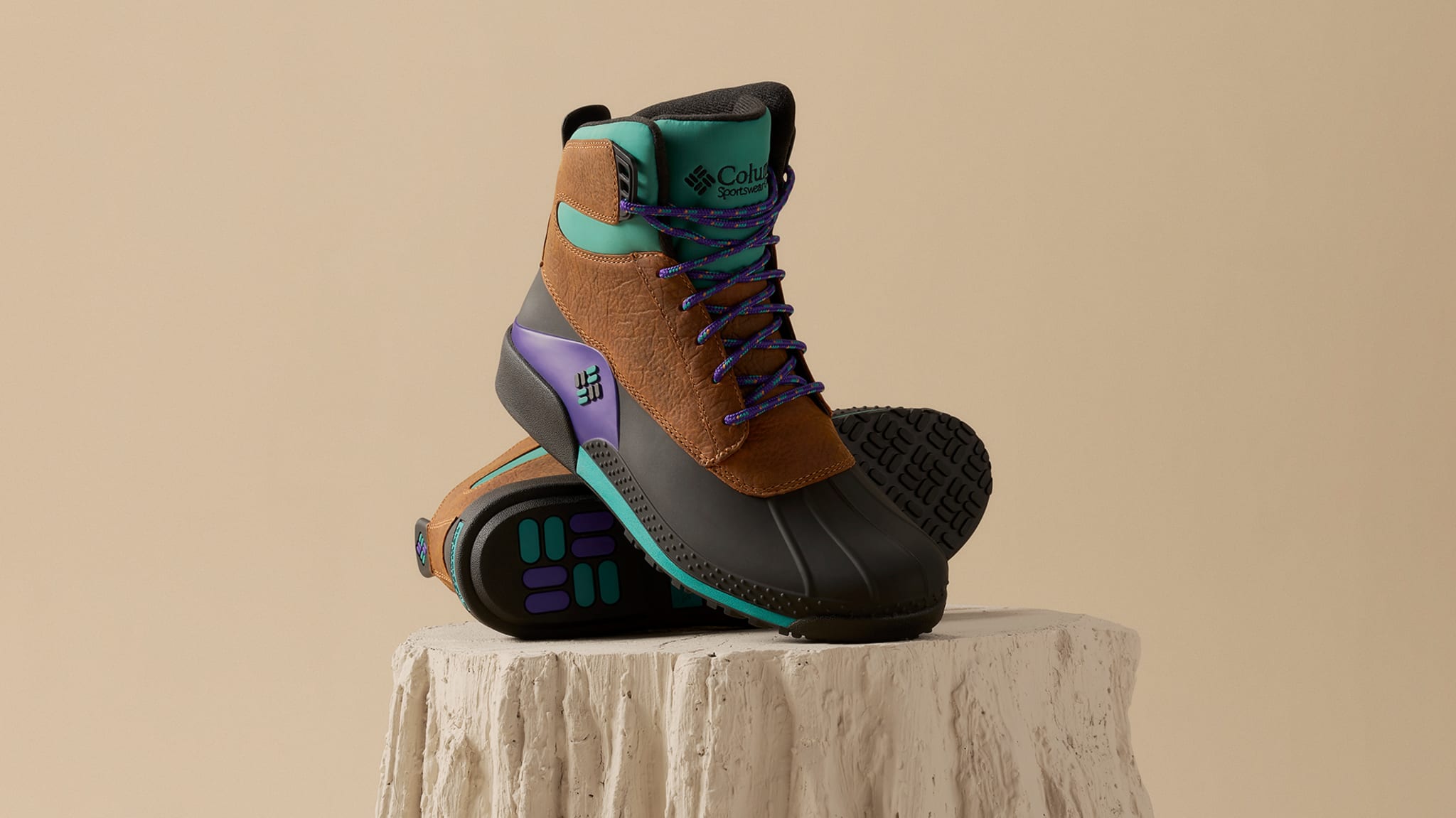 Brown and black Columbia hiking boots with purple and teal accents, displayed on a textured white pedestal.