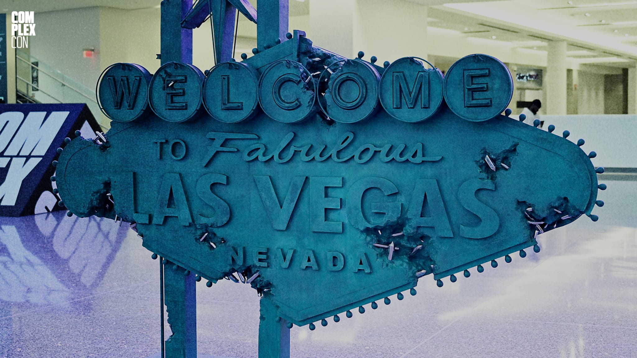A replica of the "Welcome to Fabulous Las Vegas, Nevada" sign is displayed indoors on a shiny floor, with "COMPLEX" signs in the background.