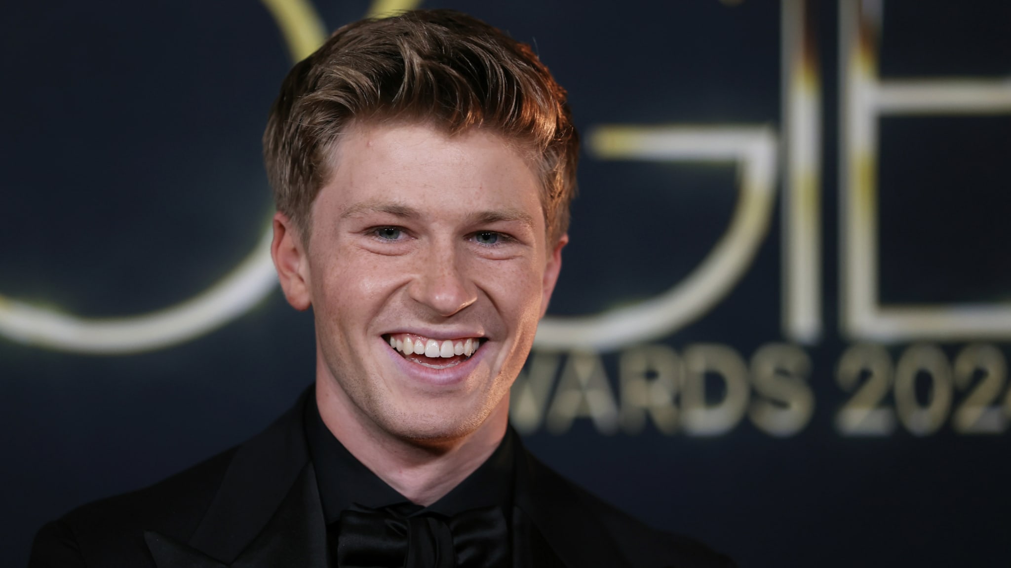 Young man in a black suit smiling at an awards event.