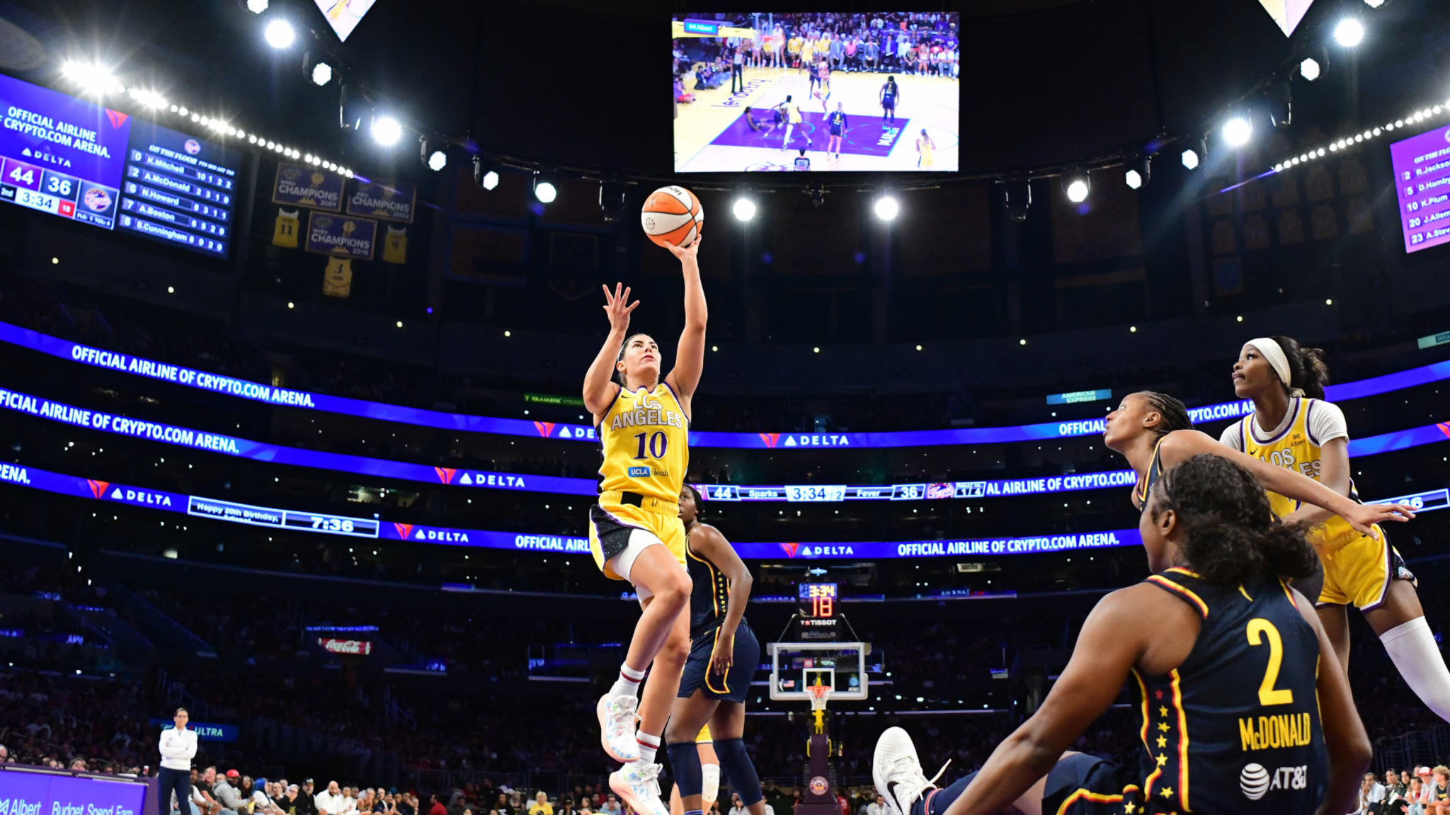 A basketball player in a yellow Los Angeles Sparks uniform leaps for a shot against the Atlanta Dream, with spectators in the background.