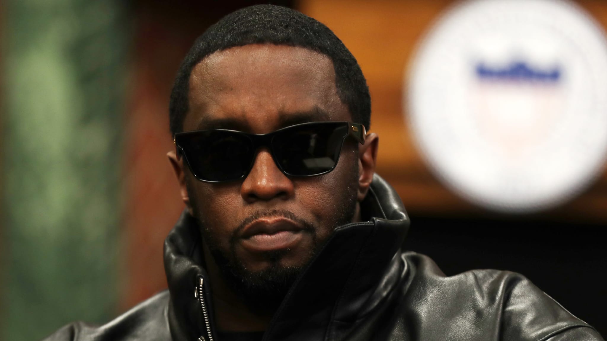 Sean "Diddy" Combs wearing sunglasses and a leather jacket, looking serious.