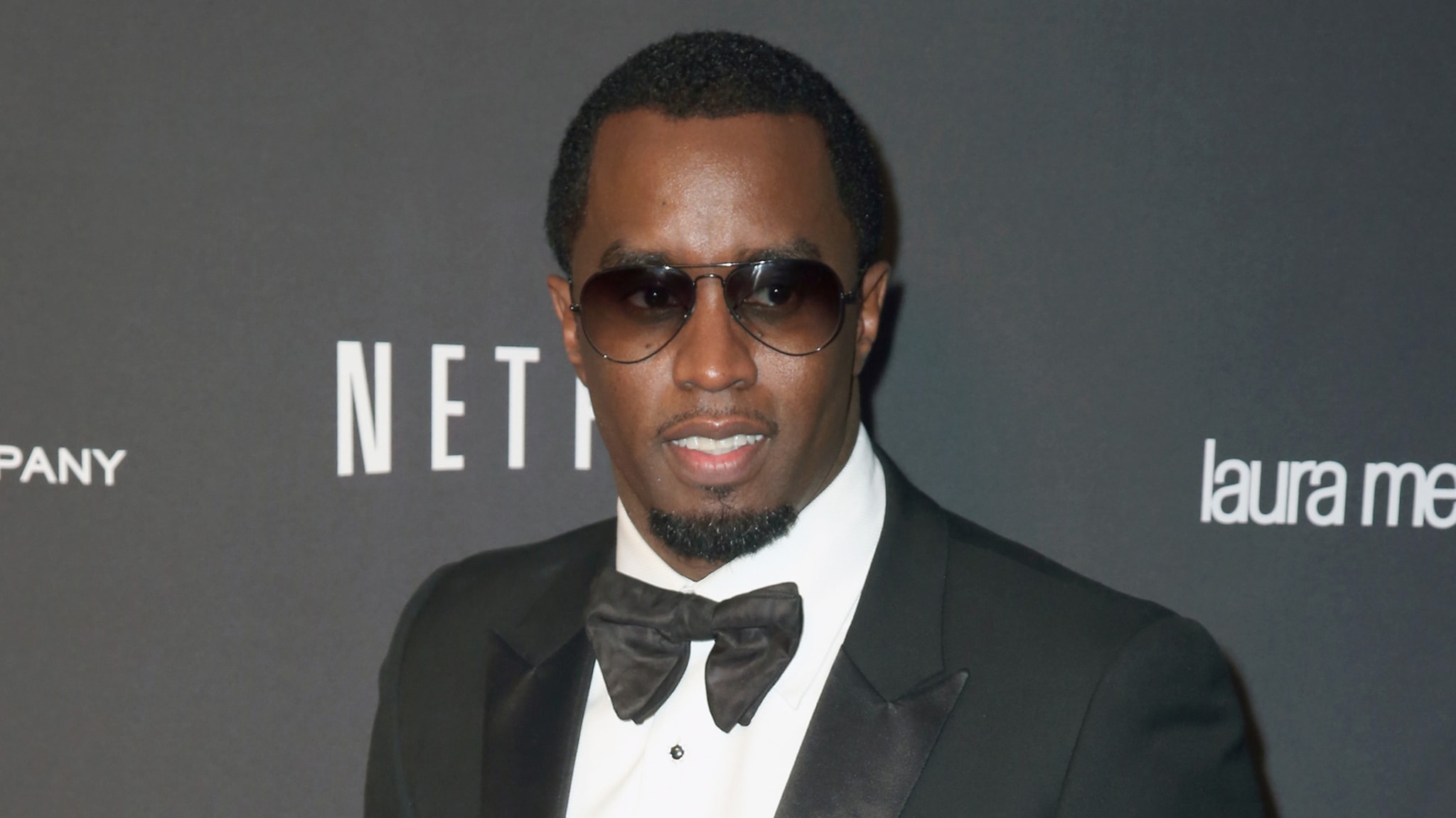 Sean "Diddy" Combs in a tuxedo and sunglasses at a Netflix event, posing on the red carpet.