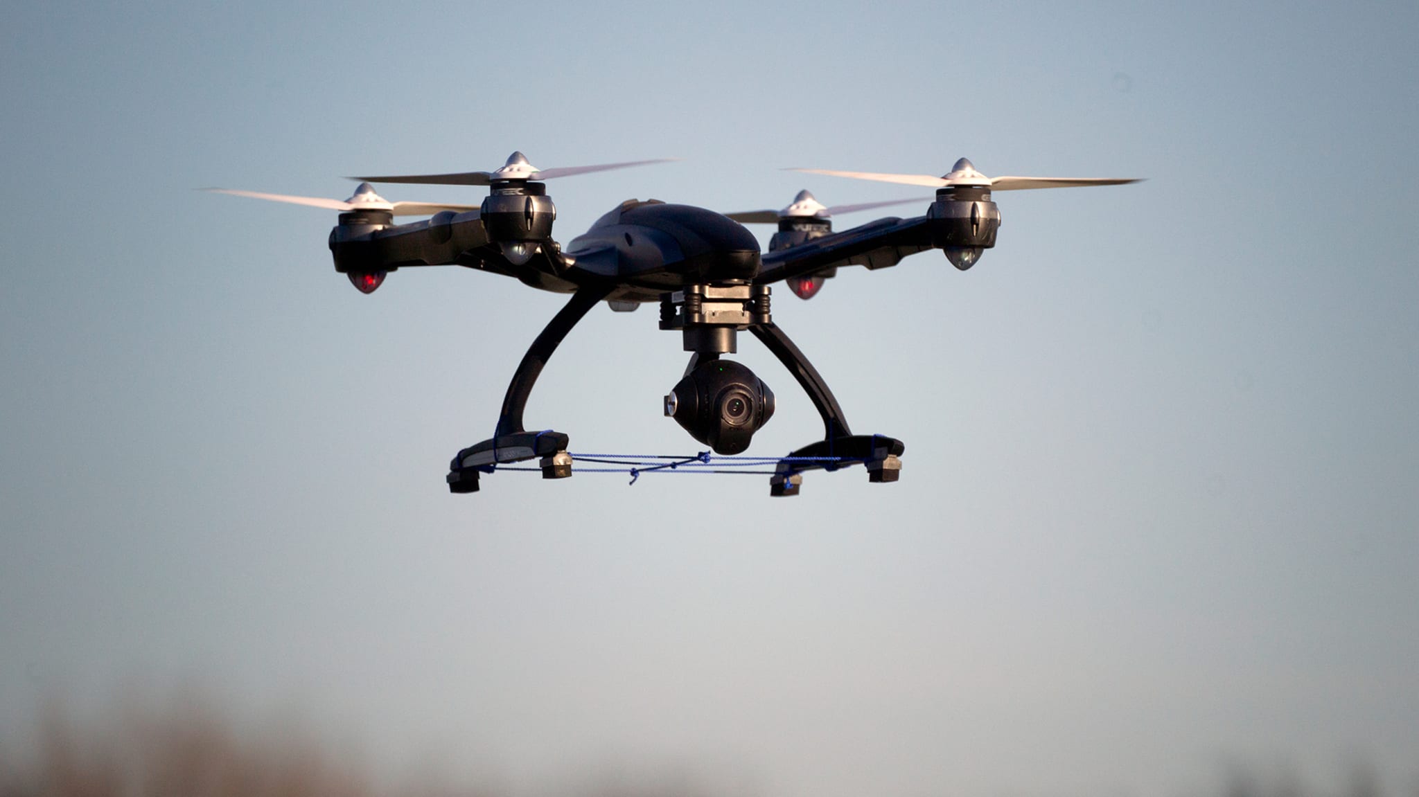 A drone with four propellers hovering in the sky, equipped with a camera underneath.