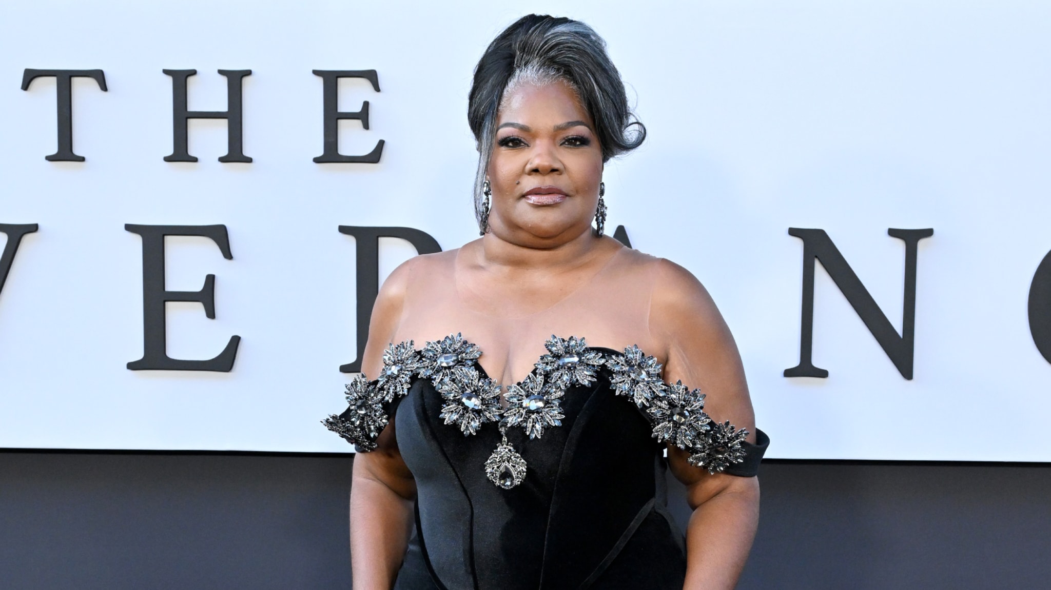 Mo'Nique in a black gown with floral embellishments, posing at an event.