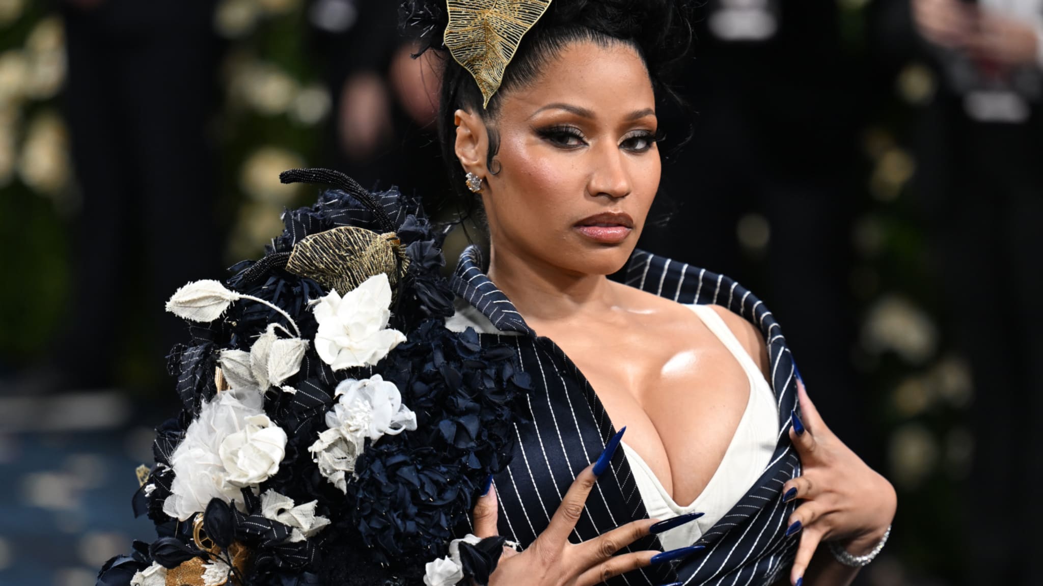 Nicki Minaj at an event, wearing a floral and pinstriped outfit with bold accessories and an elaborate hairstyle.