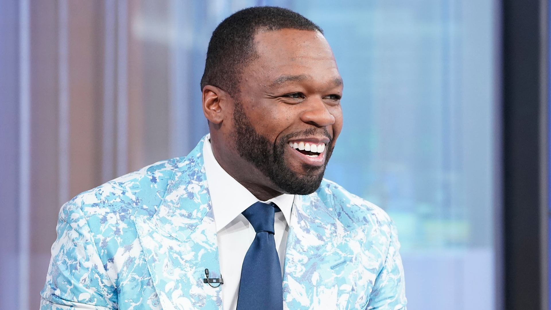Rapper 50 Cent in a blue patterned suit, smiling during an interview.